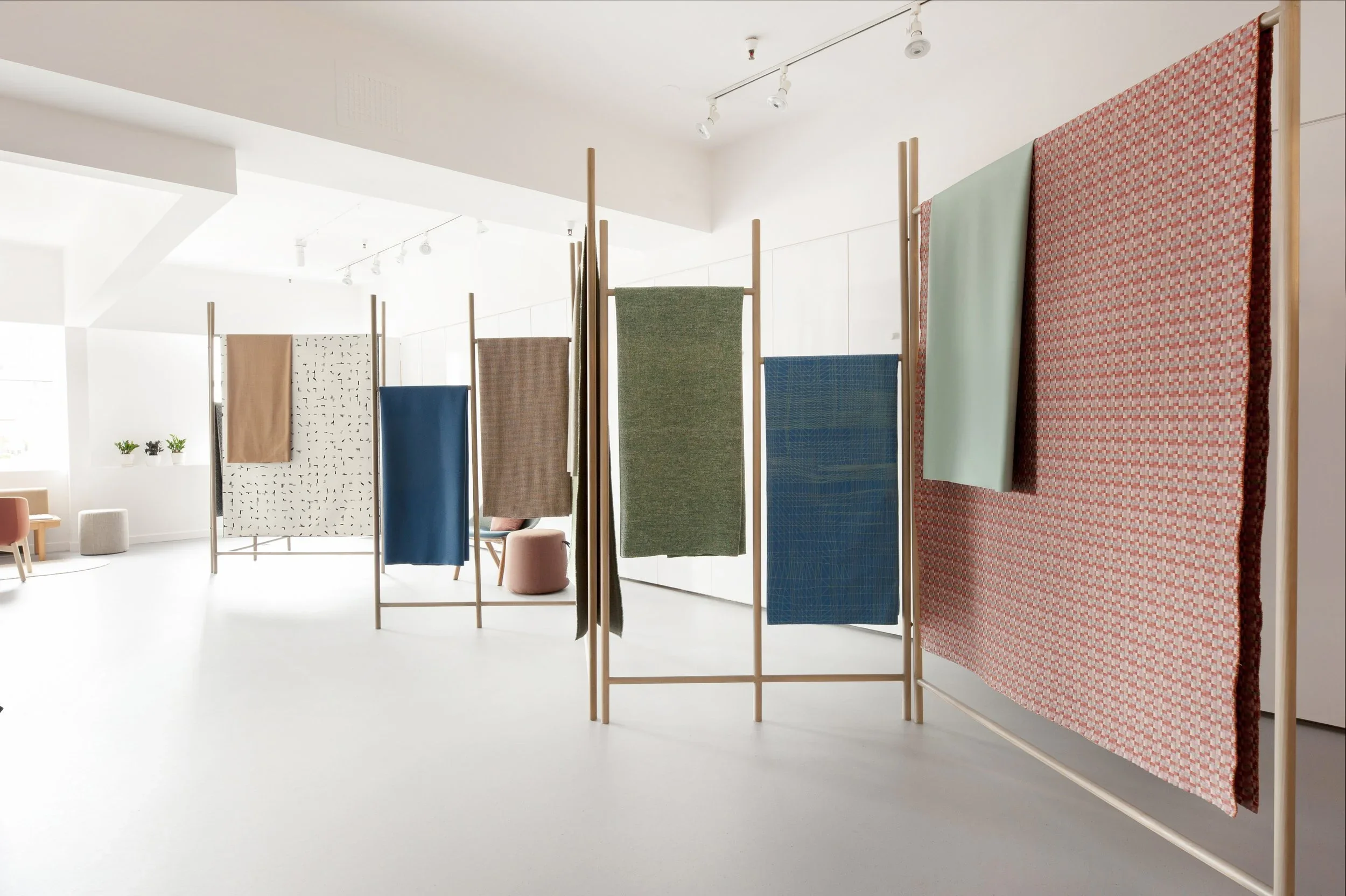 Display of colorful textiles hung on wooden frames in an art gallery with white walls and minimal decor.