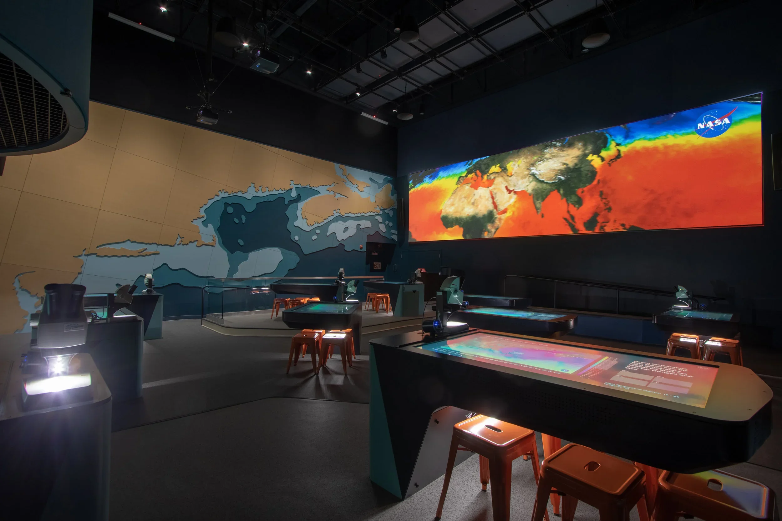 Educational exhibit with interactive displays, large world map, and a panoramic screen showing a climate map.