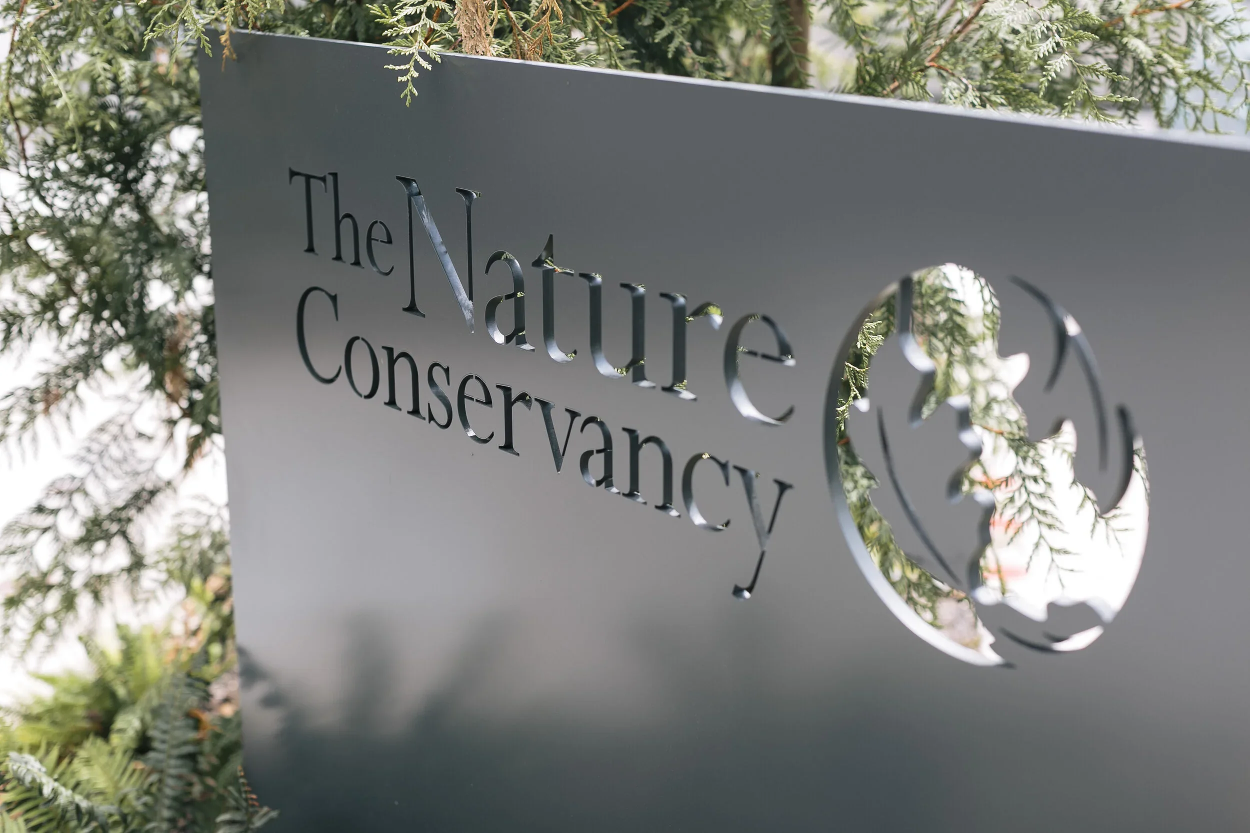 A metal sign with the words "The Nature Conservancy" cut out, surrounded by green foliage.