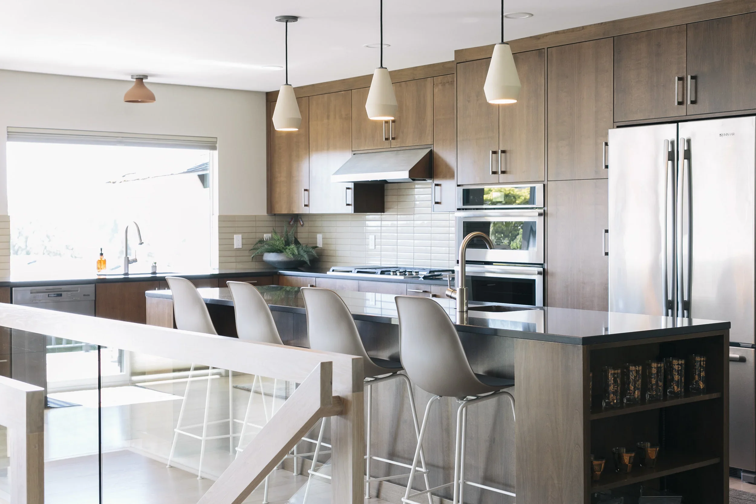 Modern kitchen with wooden cabinets, stainless steel appliances, a large window, and a kitchen island with four white chairs.