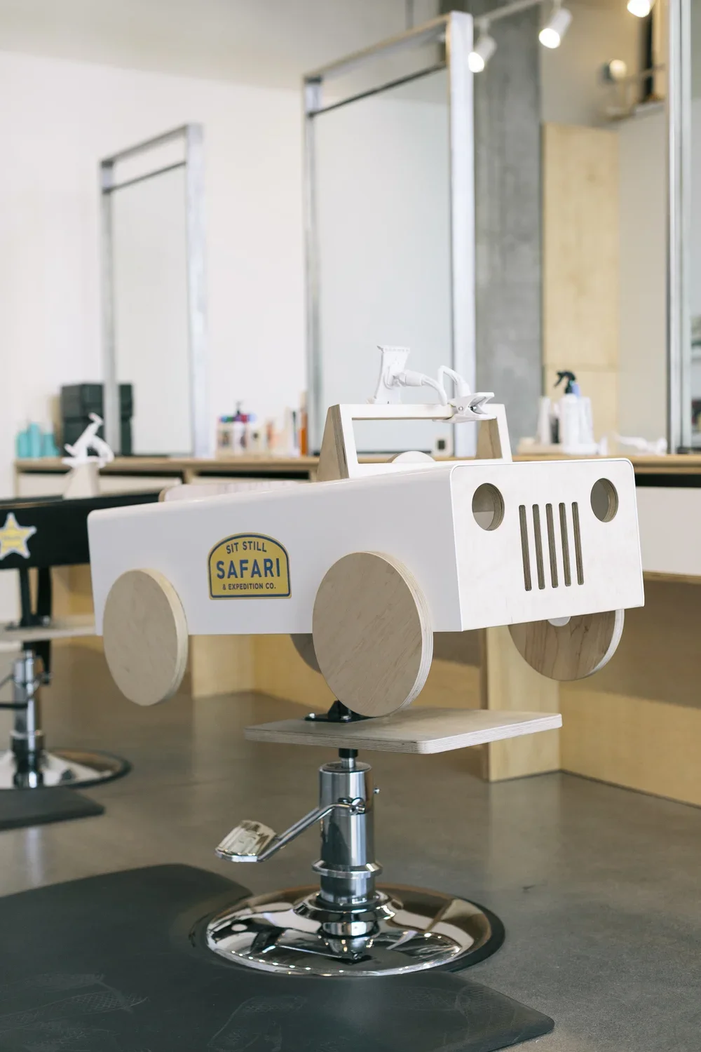 Wooden toy car with a safari expedition sign on the side, placed on a salon chair in a modern interior space.