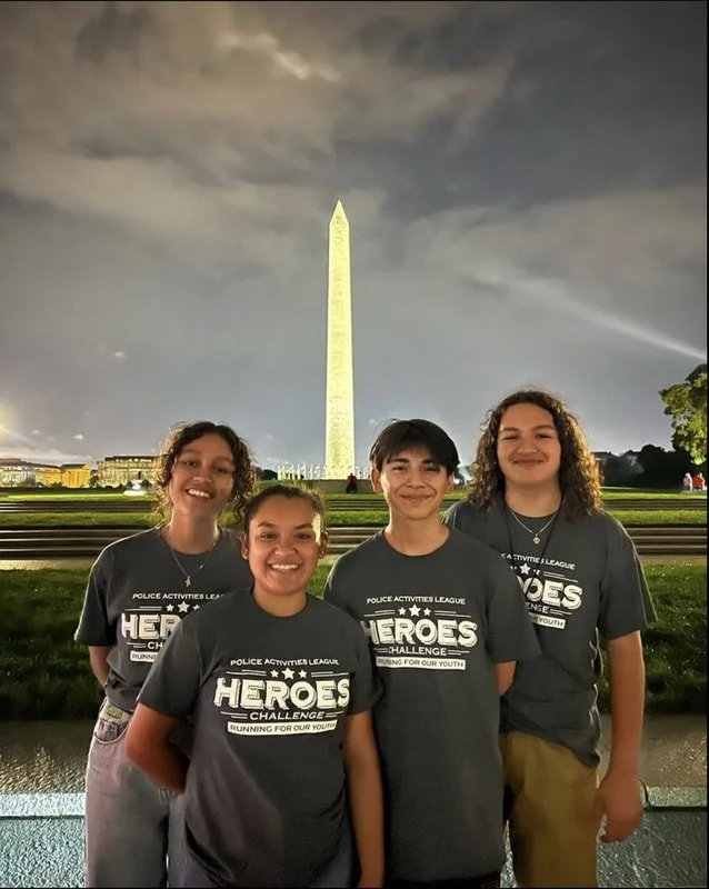 Four young people standing in front of the Washington Monument at night, smiling with a cloudy sky behind them.