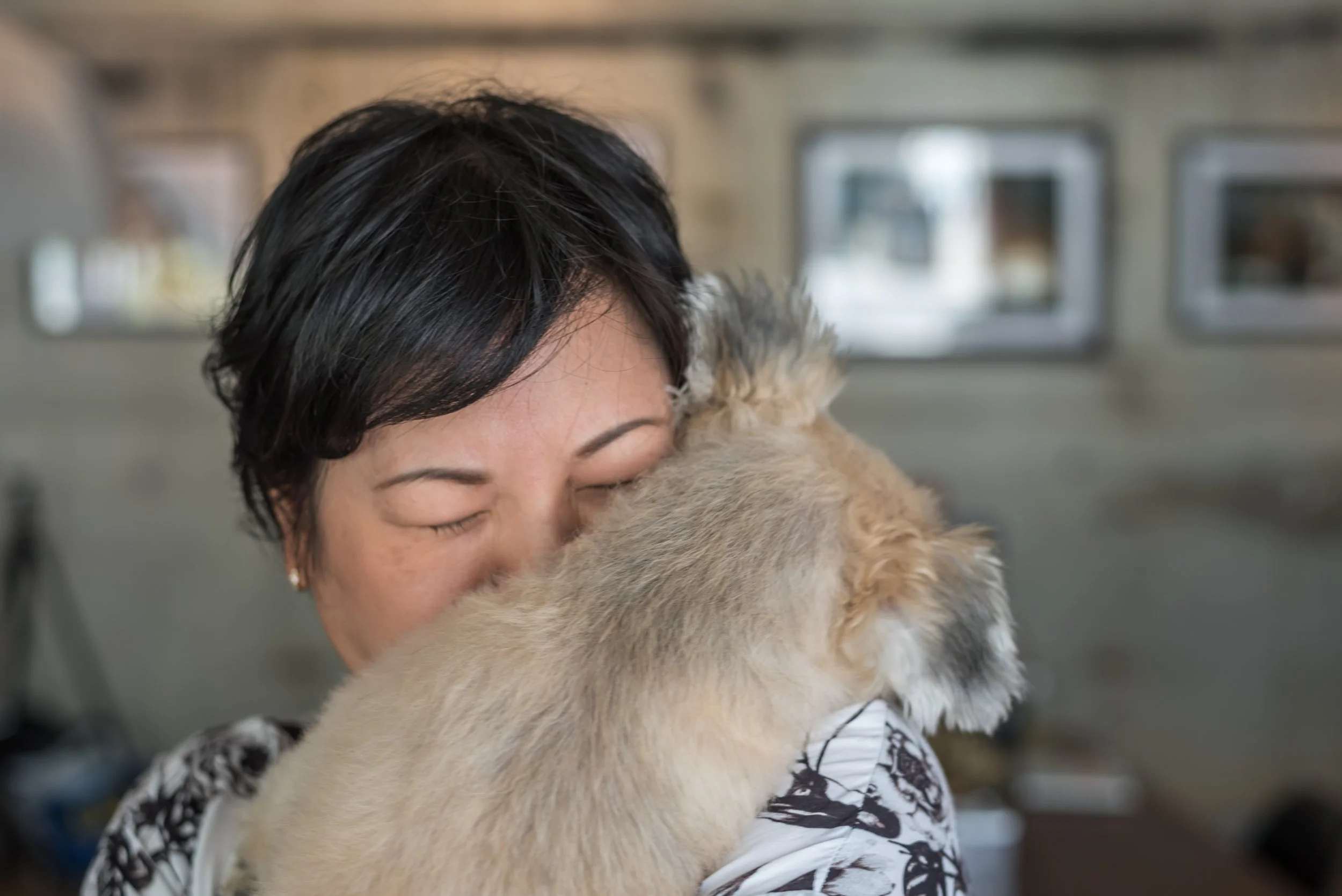 A woman with short black hair hugging a golden retriever puppy inside a building.
