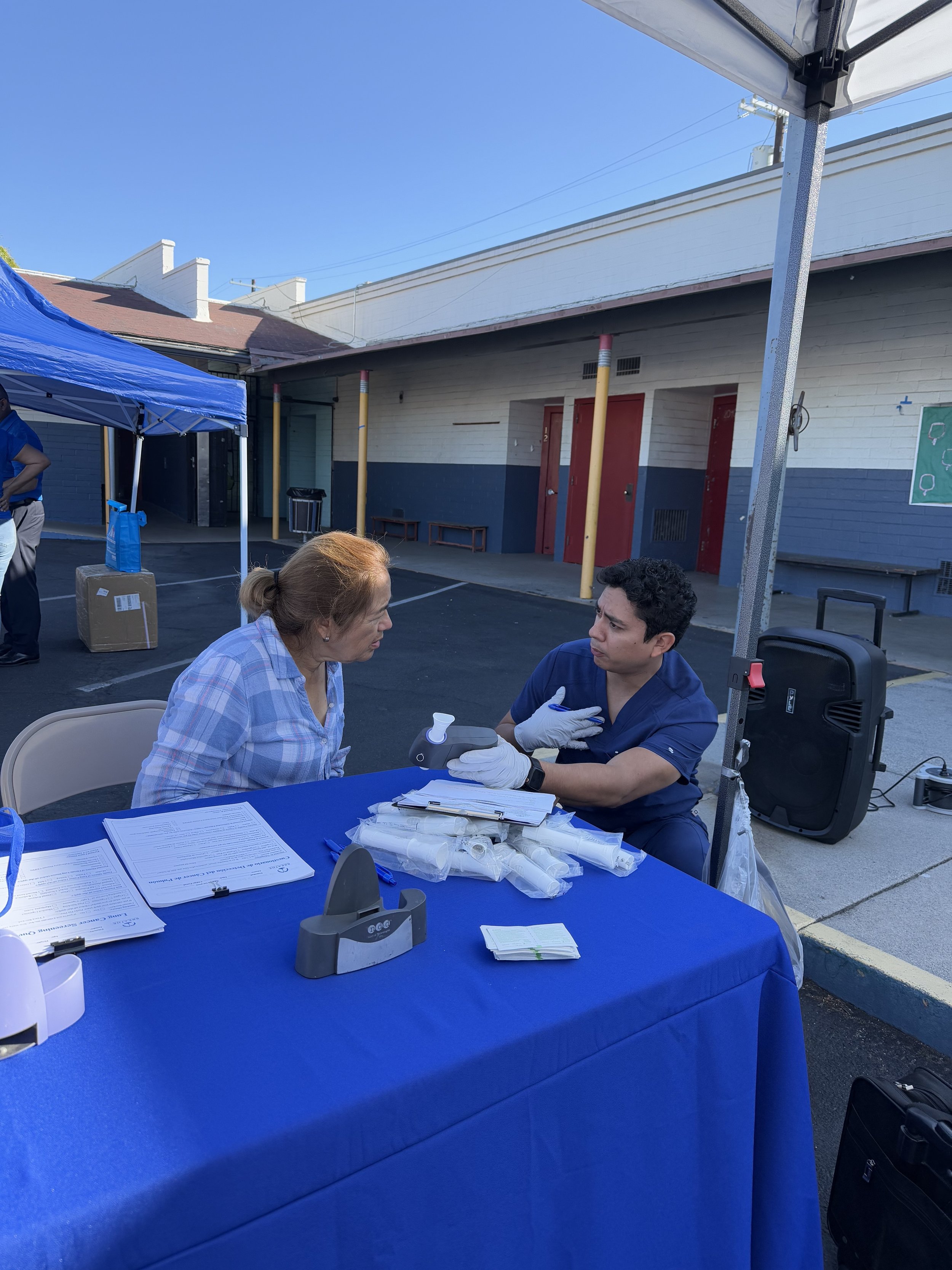 Medical professionals conducting a COVID-19 testing event outdoors with a blue canopy and a table with paperwork.