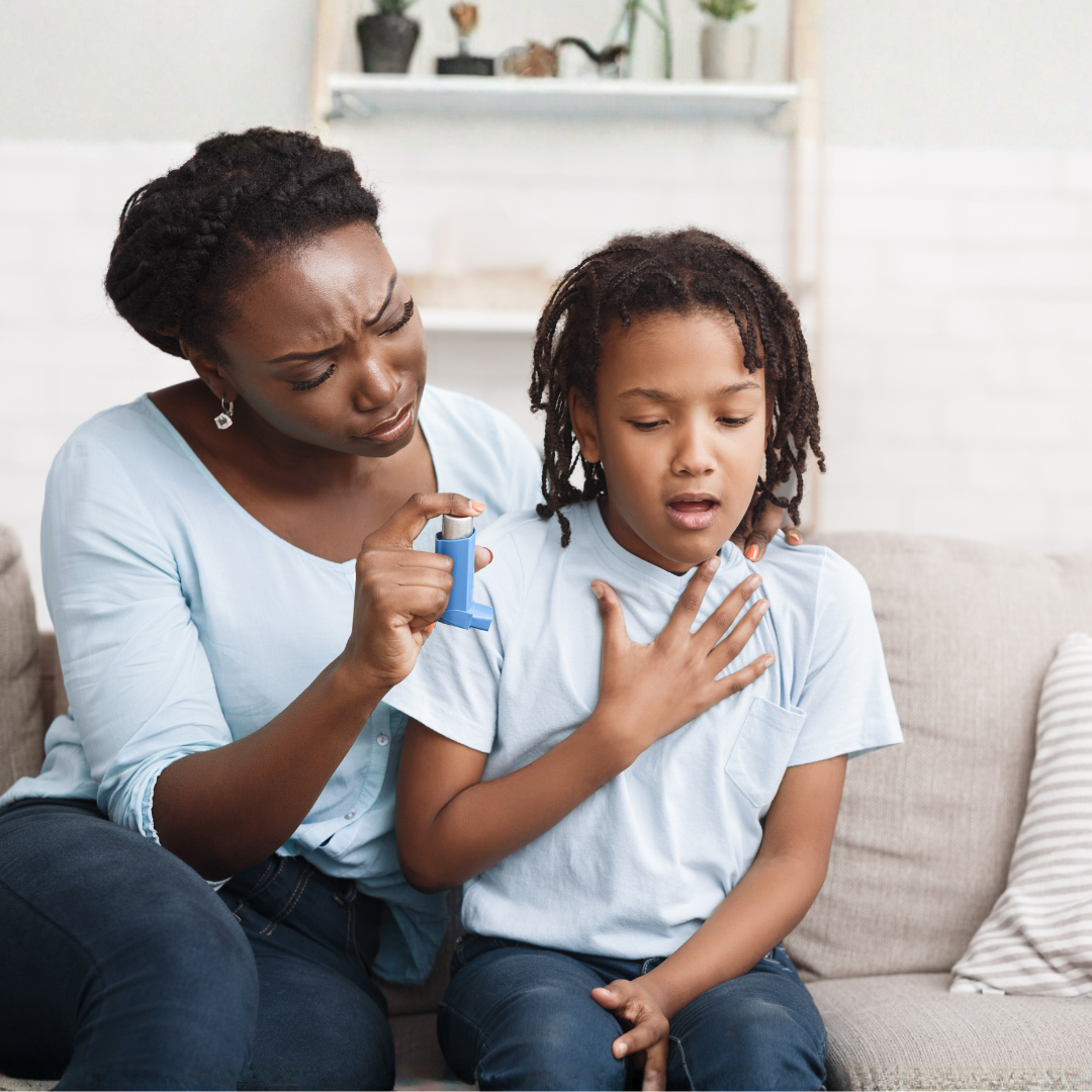 A woman administering an inhaler to a young girl showing signs of difficulty breathing, sitting on a couch in a living room.