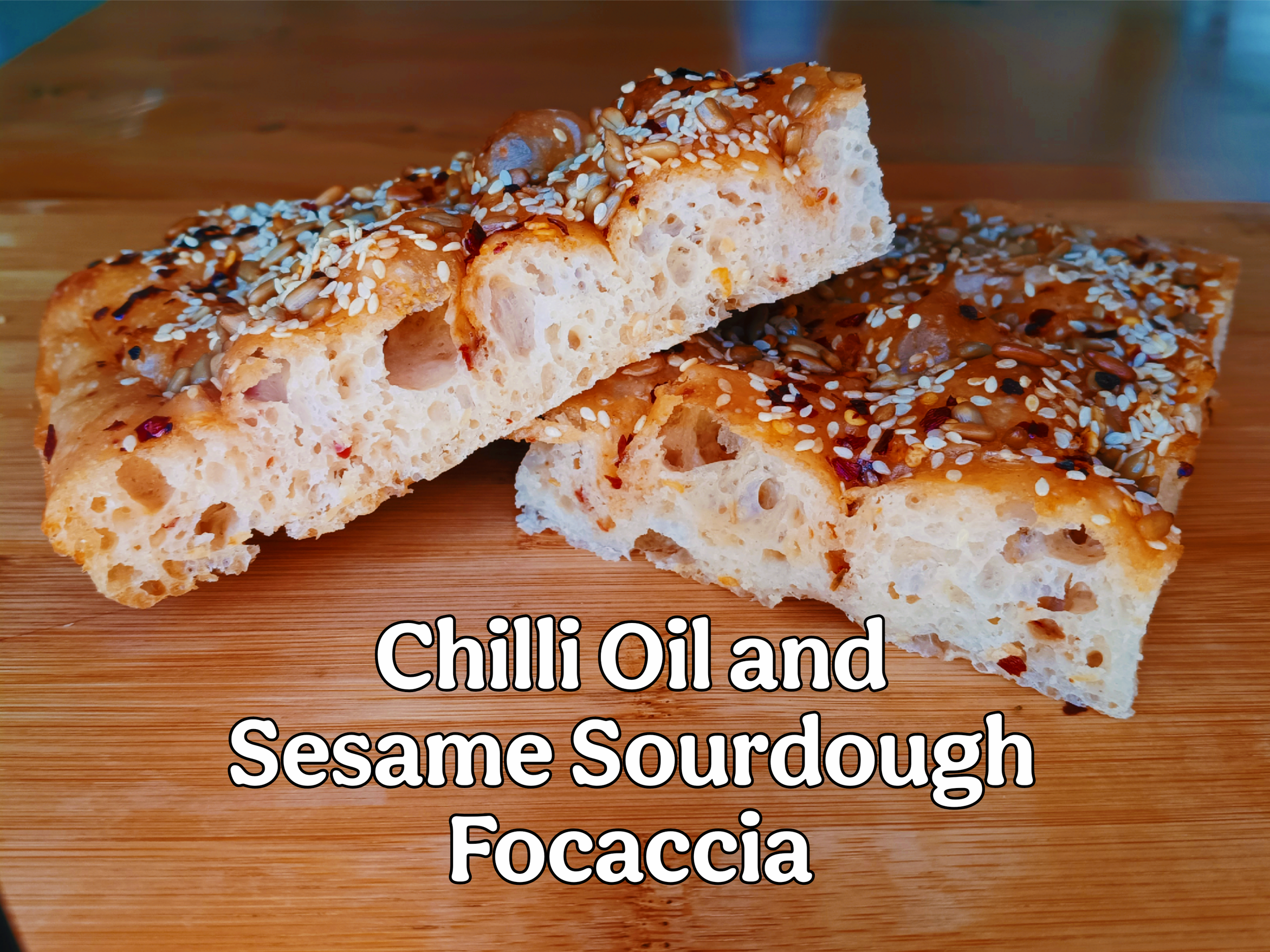 Cross cut section of chilli oil and sesame sourdough focaccia showing pockets of chilli oil inside and toasted sesame seeds and sunflower seeds on top.
