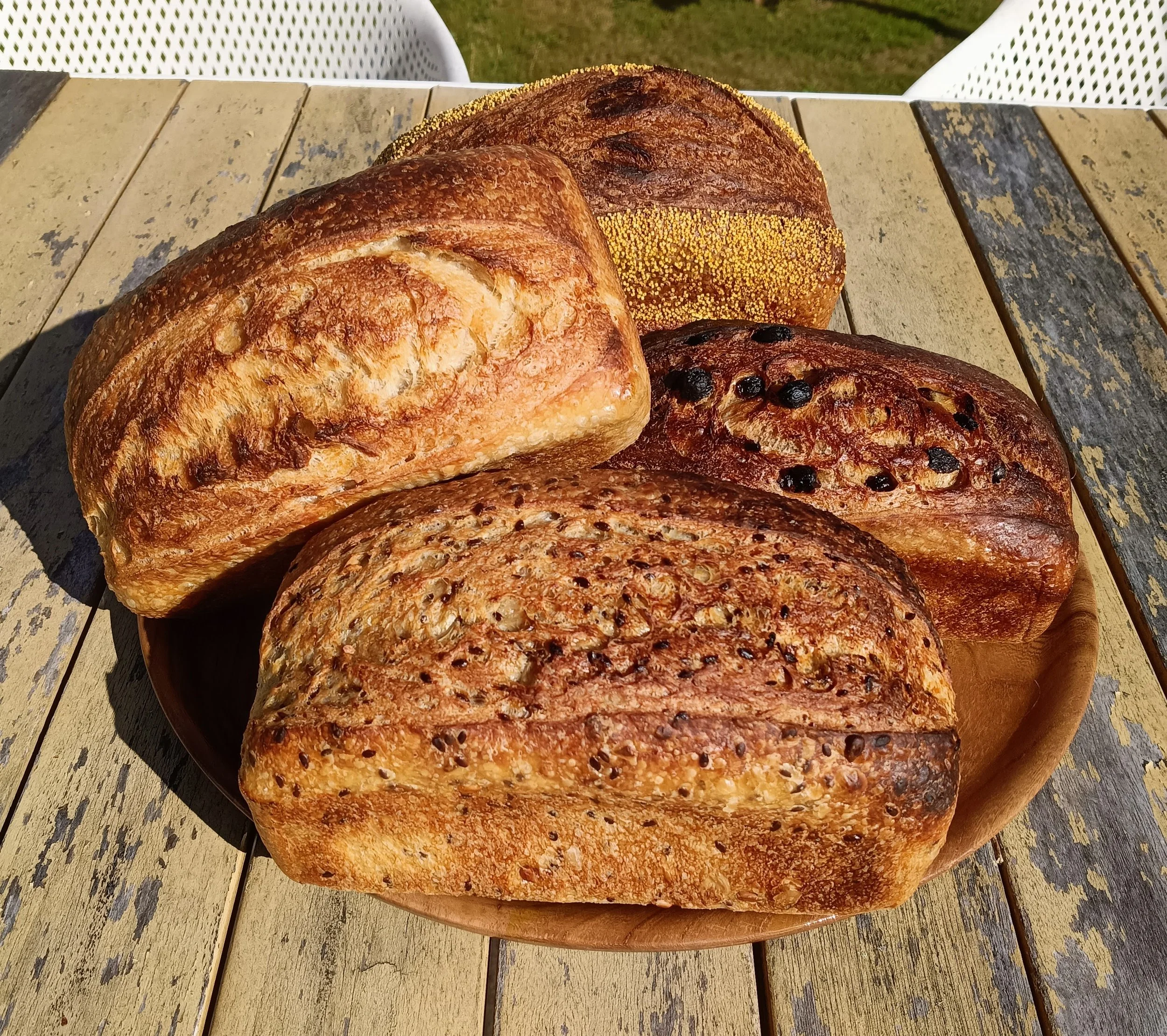 Four different flavoured sourdough loaves on a platter outdoors, classic, seeded, sultana, Marmite.