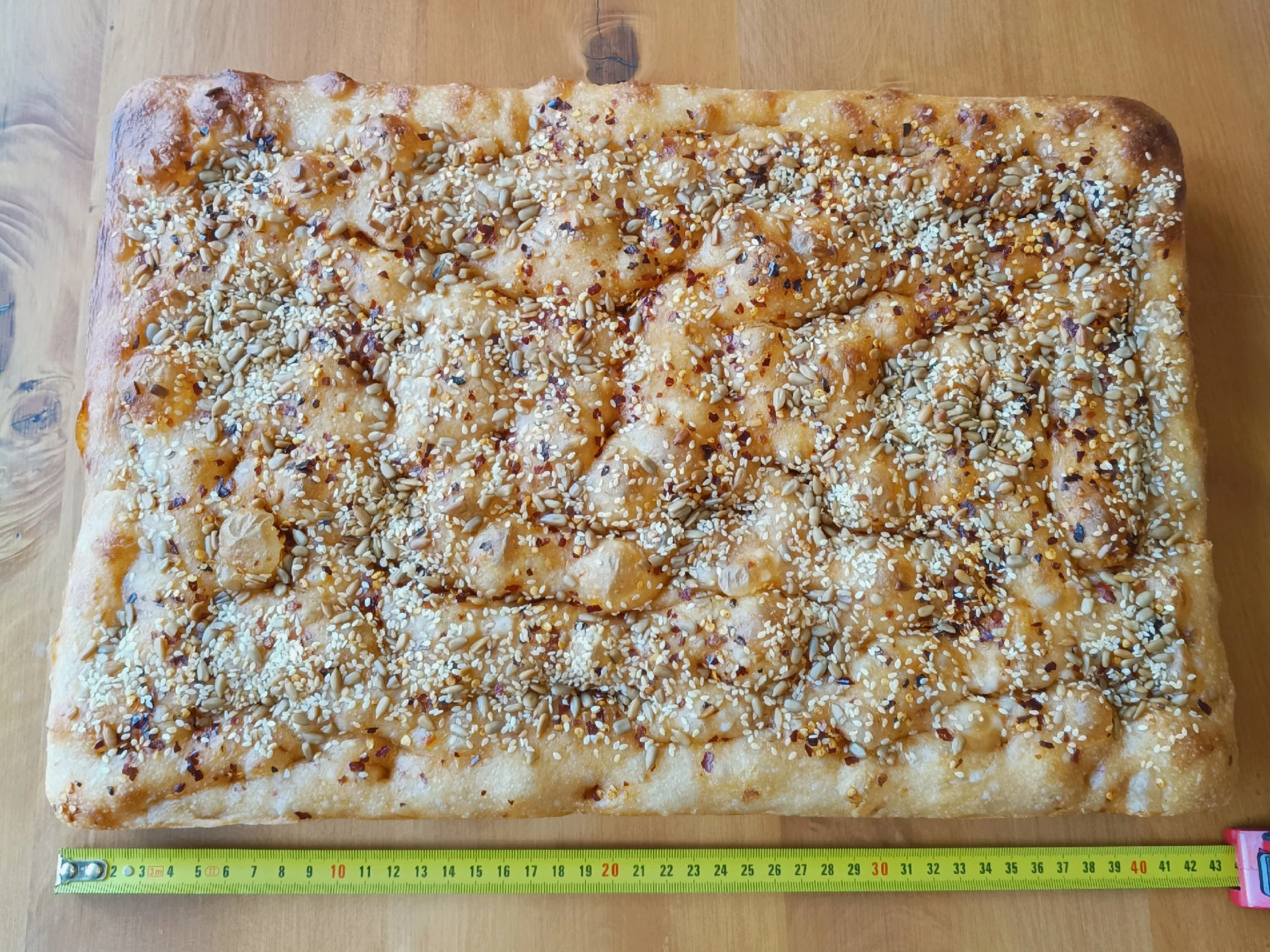 Whole sourdough focaccia slab along with a measuring tape showing a full slab is more than 40cm wide by at least 30cm.