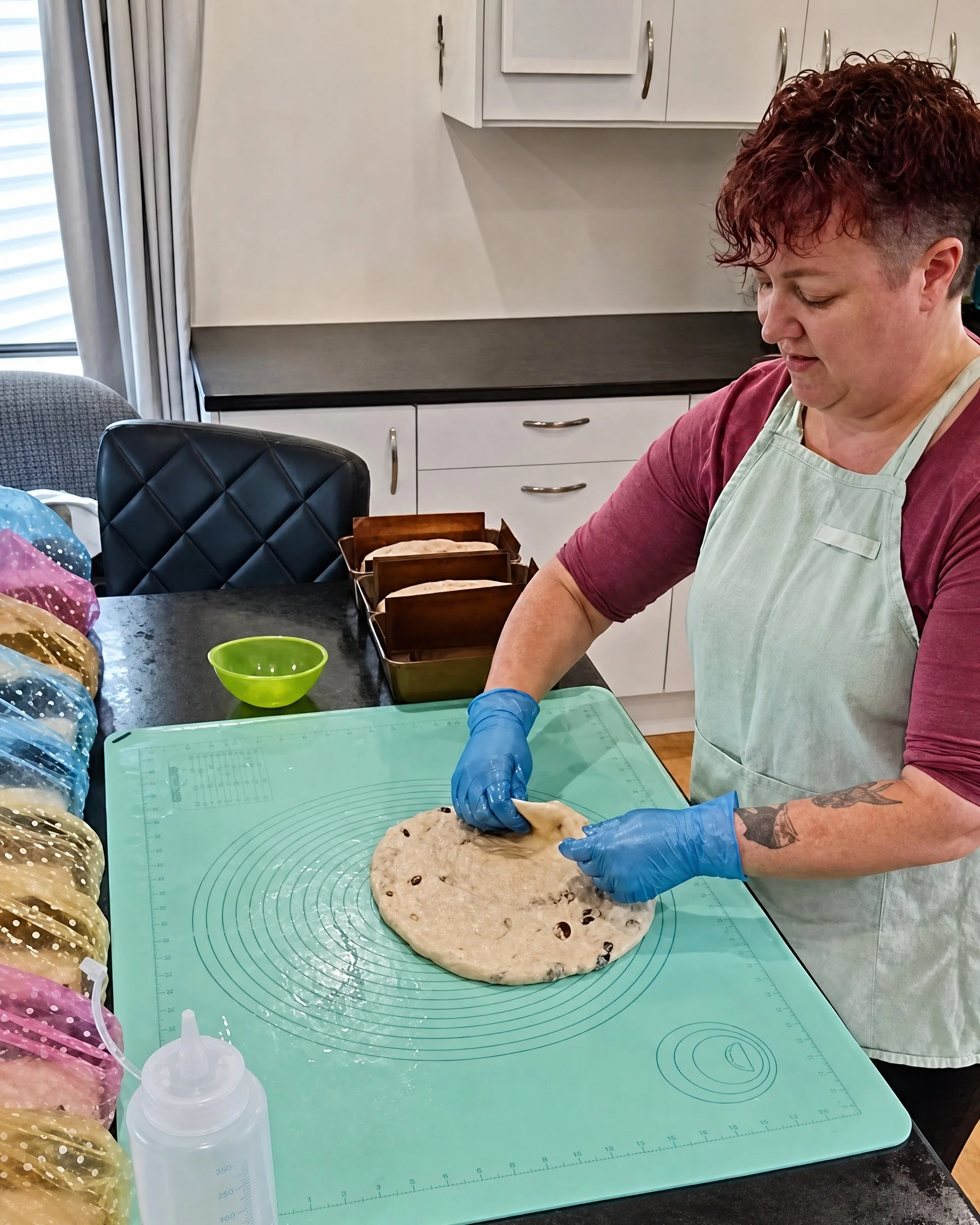 Meg the baker at workbench shaping sultana loaf to go in tin. Pre tinned loaves visible.