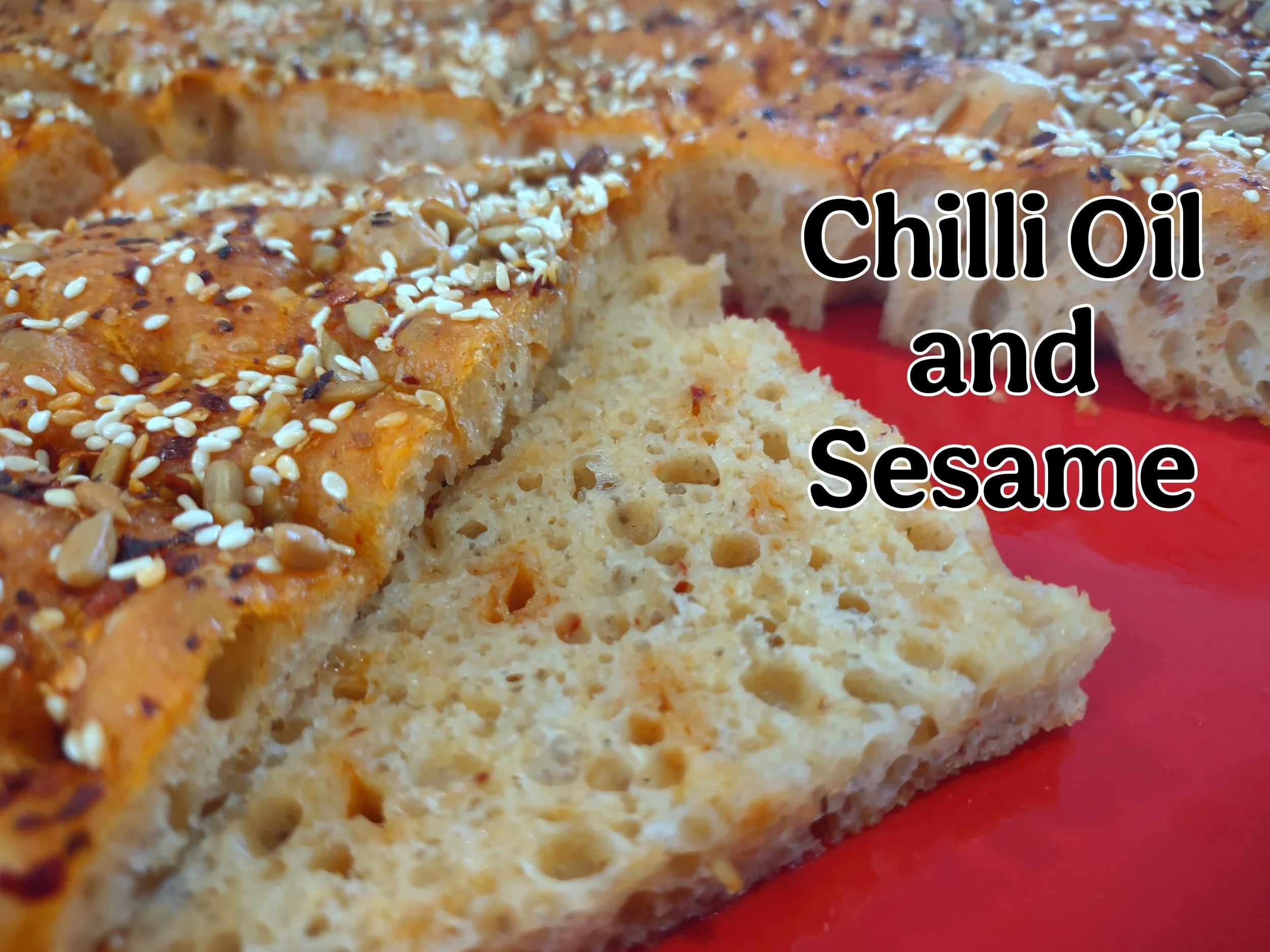 Sliced open portion of chilli oil and sesame sourdough focaccia bread showing pockets of homemade chilli oil throughout and toasted seeds on top.