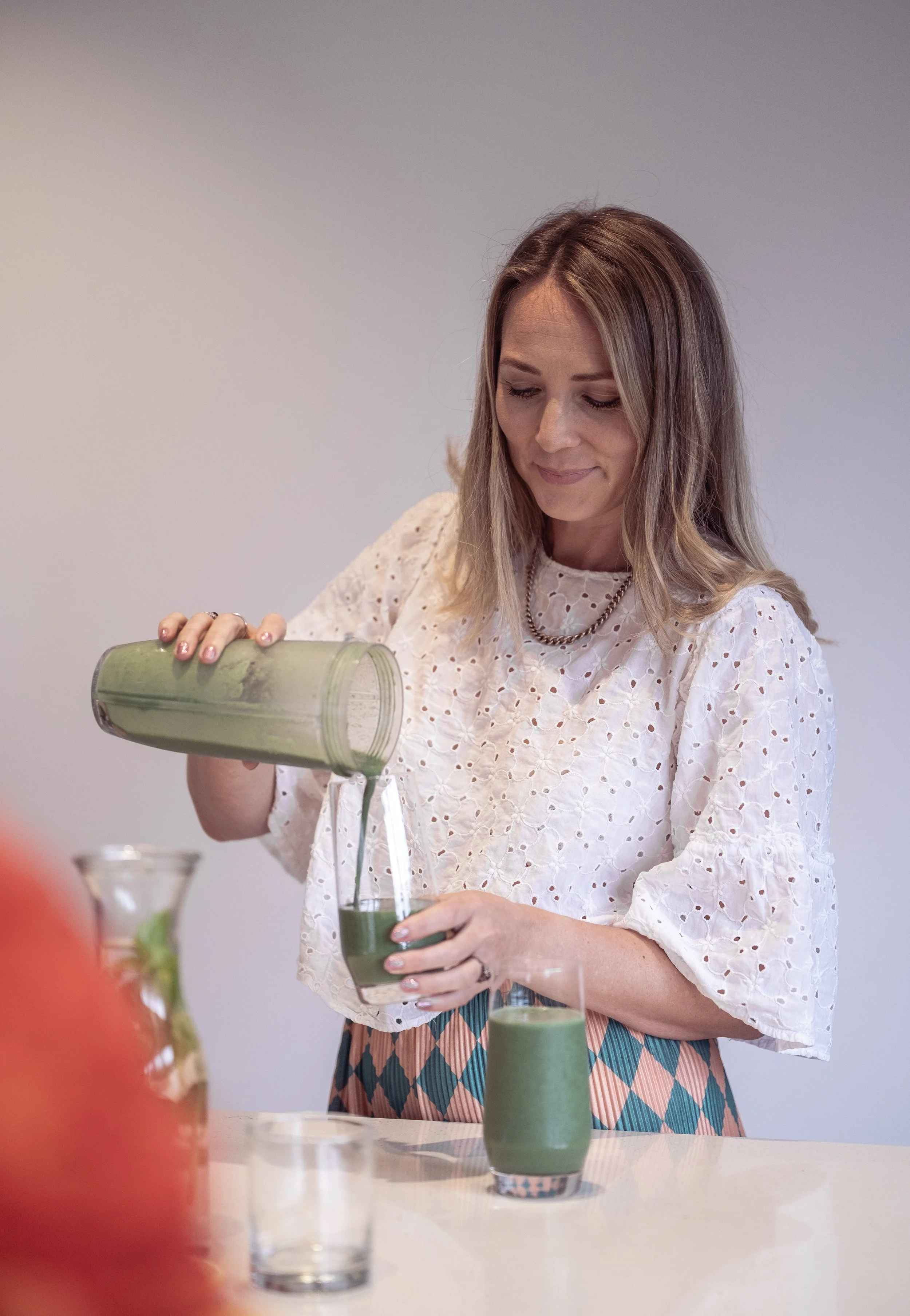 A woman pouring green smoothie from blender into a glass.