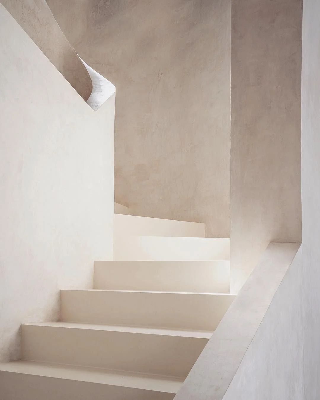 Minimalist staircase with white steps and beige walls, featuring sharp angles and clean lines.