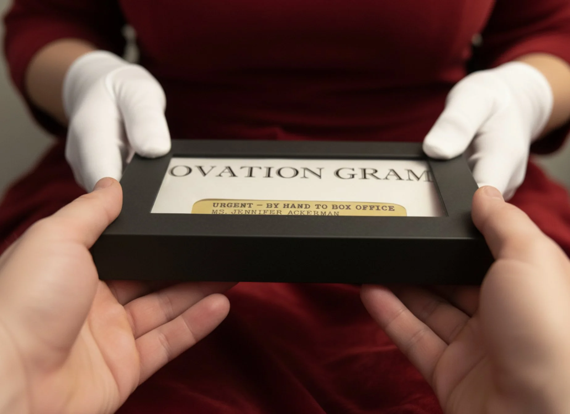 Two hands holding a black box with a white envelope holding an  Ovation Gram in a custom black keepsake box..