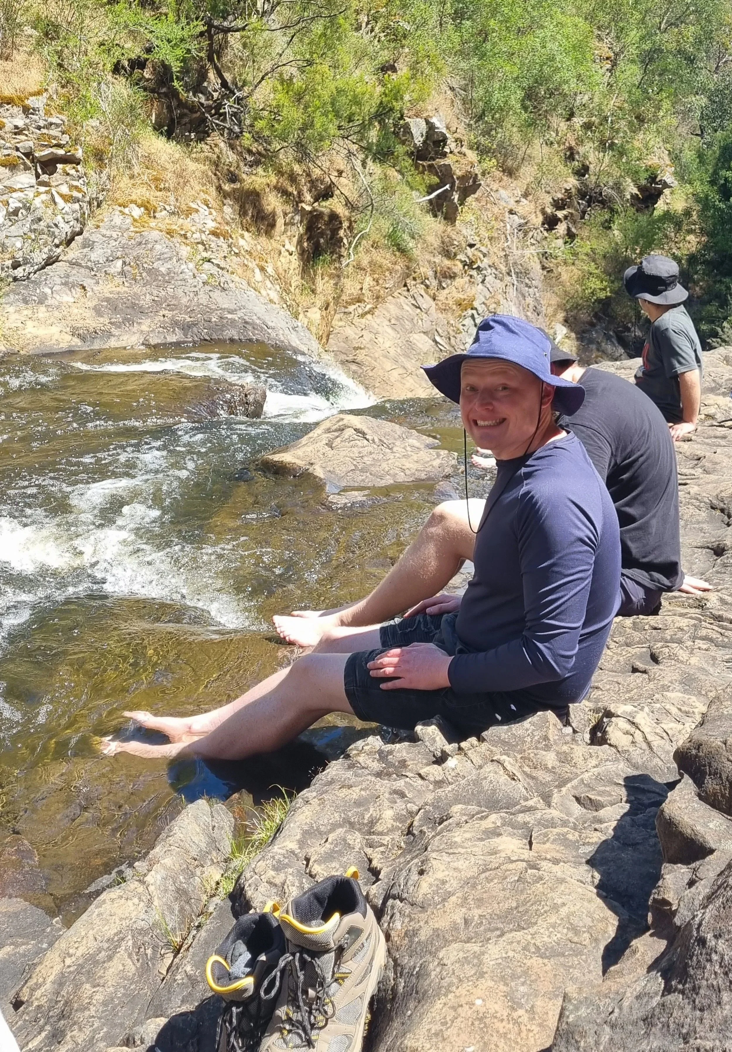 People sitting on rocks by a river, relaxing and enjoying the outdoors.