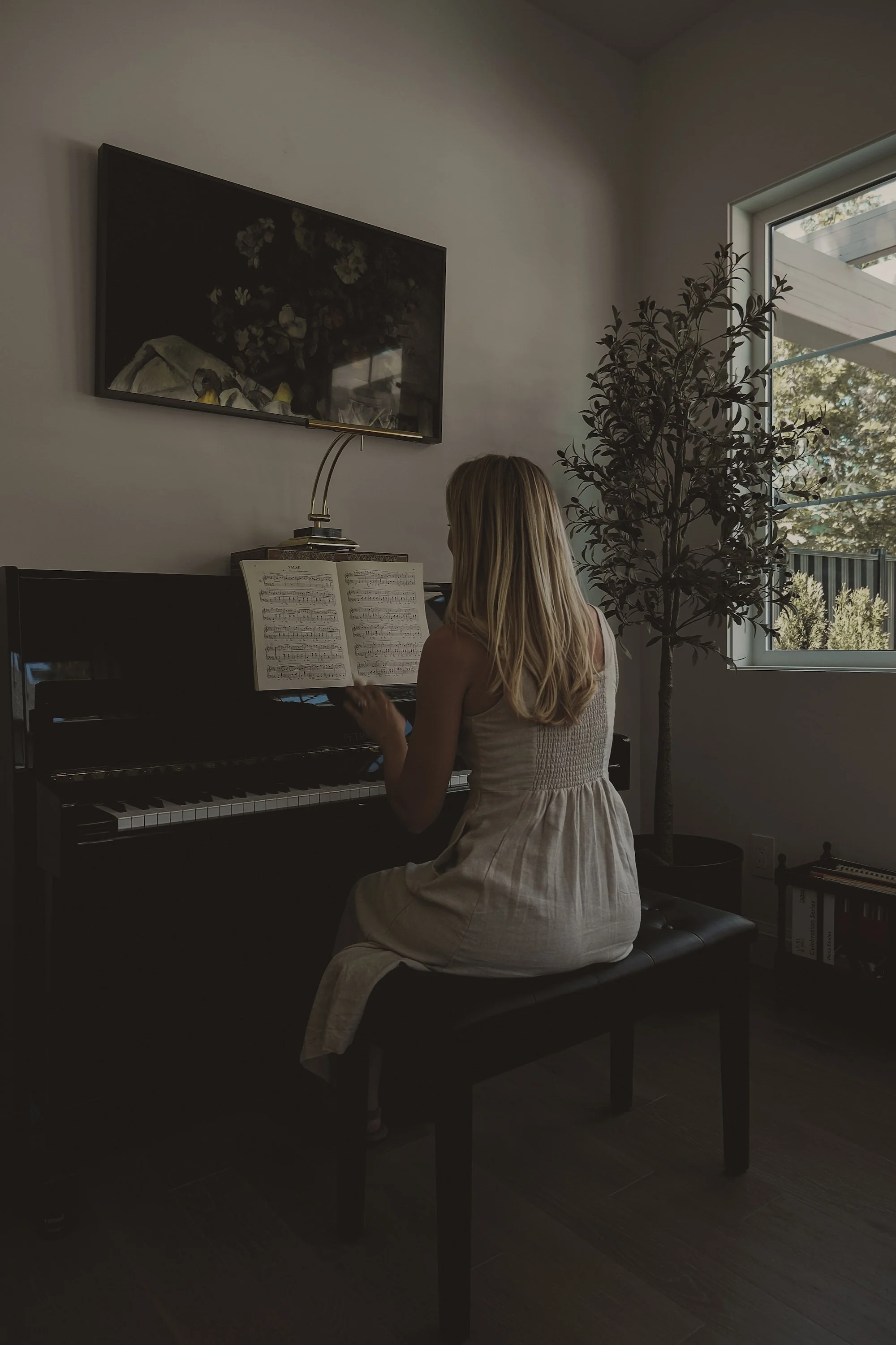 A young girl playing the piano in a well-lit room with a window, a potted plant, and a painting on the wall.