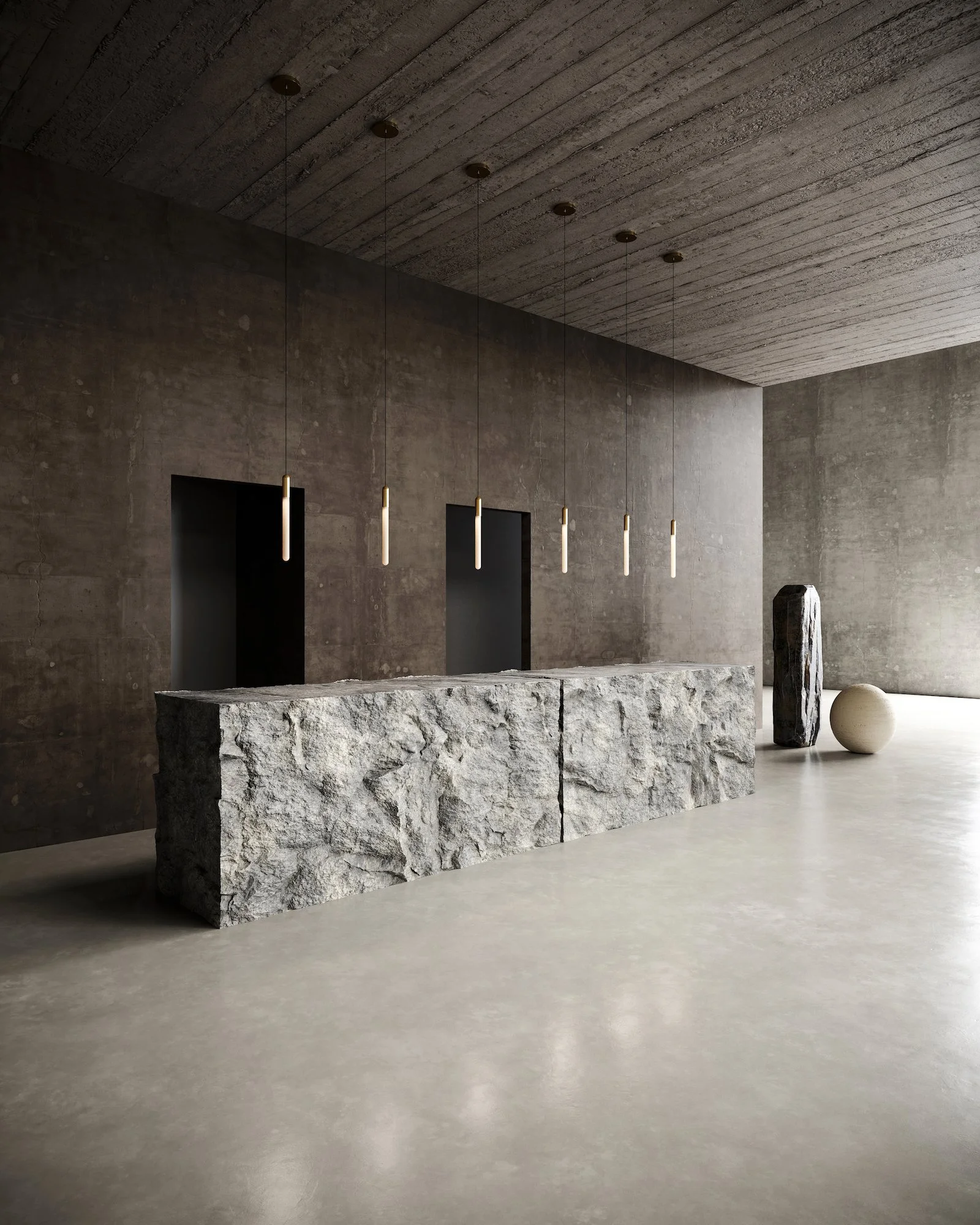 A minimalist interior with a large, rough-textured stone table in the foreground, a dark textured wall with two doorways in the background, and decorative stone sculptures to the right, with suspended pendant lights hanging from a concrete ceiling.