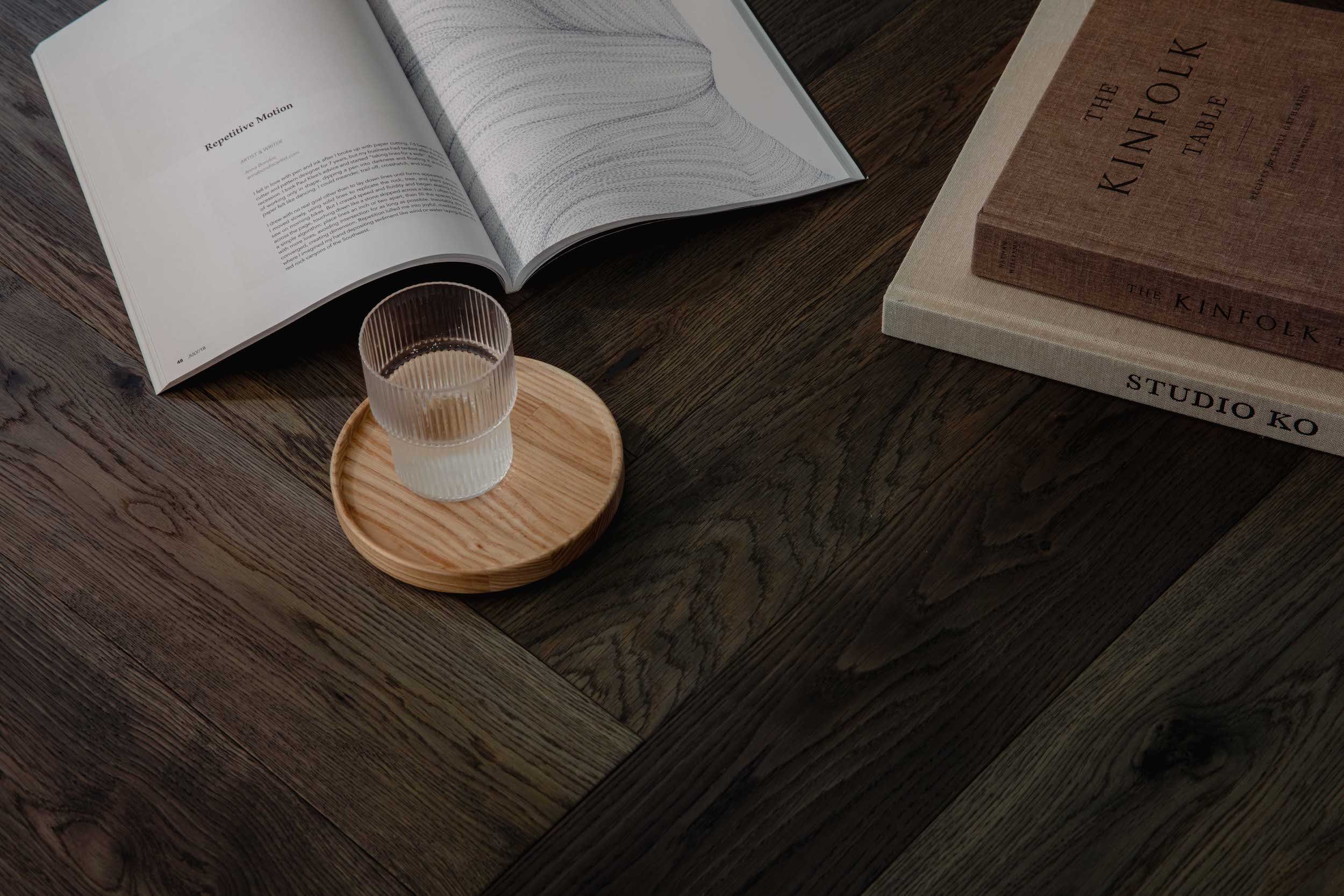A wooden table with an open book, a glass of water on a round wooden coaster, and two stacked books titled 'The Kinfolk Table' and 'Studio Ko'.