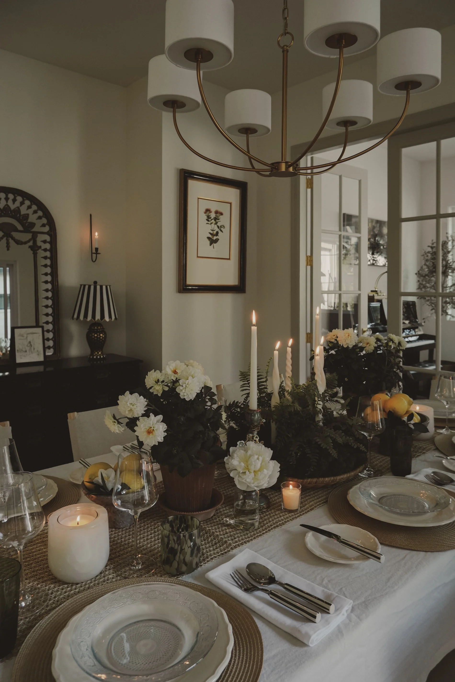 Elegant dining table set with white plates, wine glasses, cutlery, candles, and floral centerpieces, in a warmly lit room