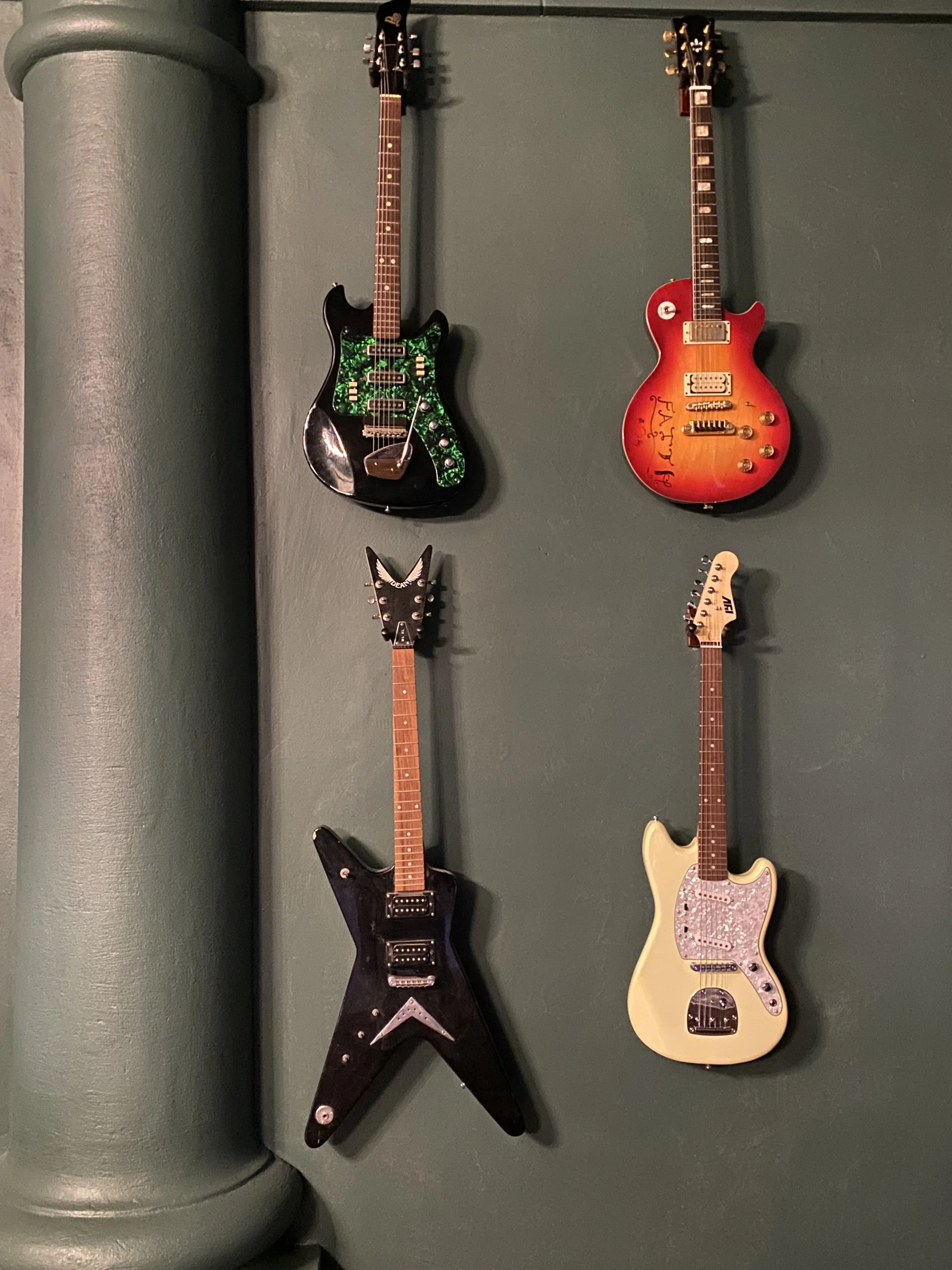 Four electric guitars hanging on a dark green wall.