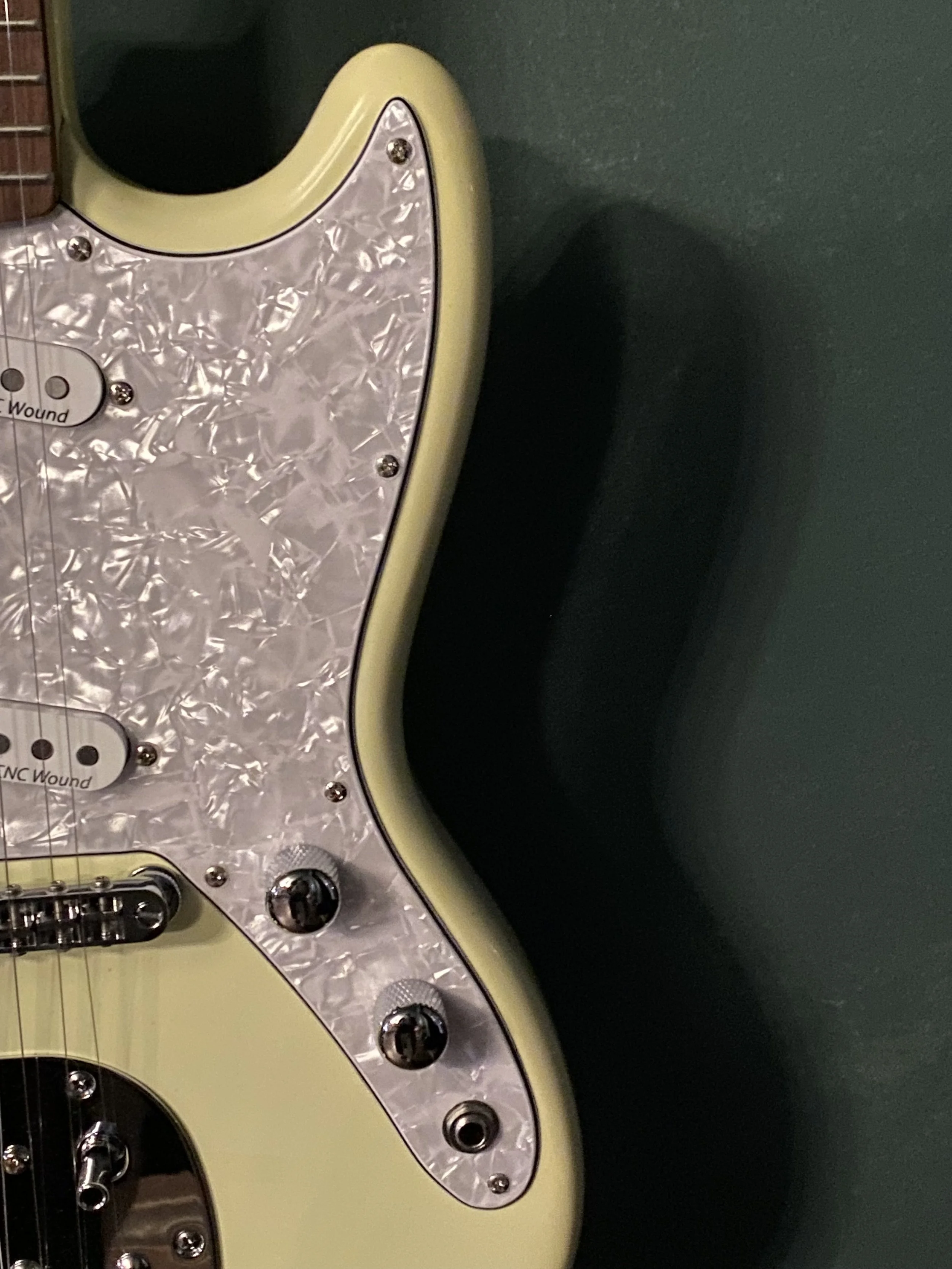 Close-up of a cream-colored electric guitar with a pearl pickguard on a dark green background.