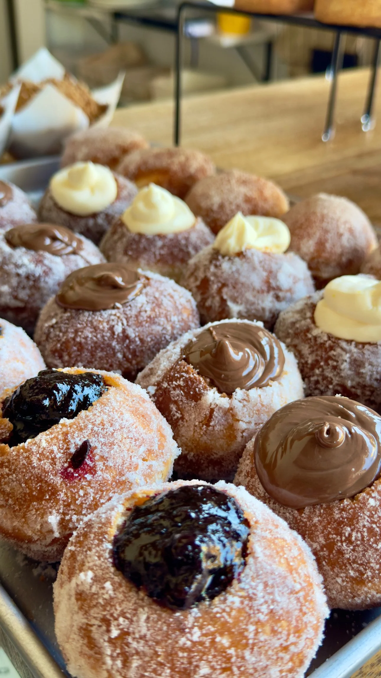 An assortment of powdered sugar-coated donuts topped with various fillings, including chocolate, custard, and fruit preserves.