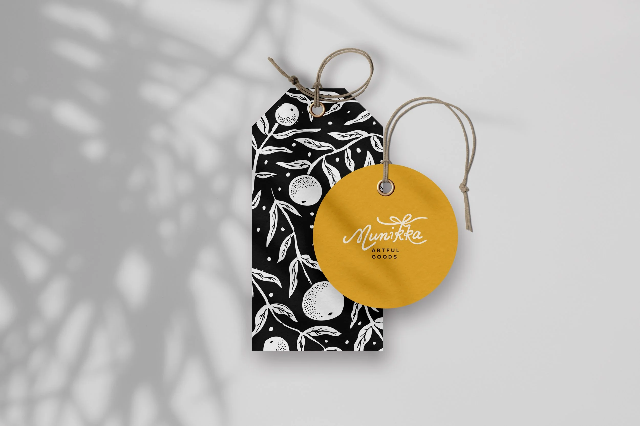 Two gift tags, one black with white botanical pattern and the other yellow with white and black lettering, hanging against a white background