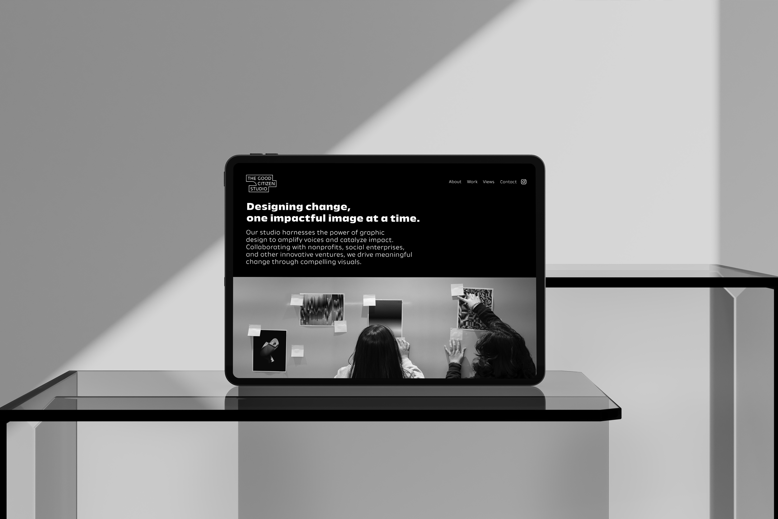 A tablet displays a website for 'The Good Citizen Studio,' with the headline 'Designing change, one impactful image at a time,' and an image of two people observing artwork on a wall.
