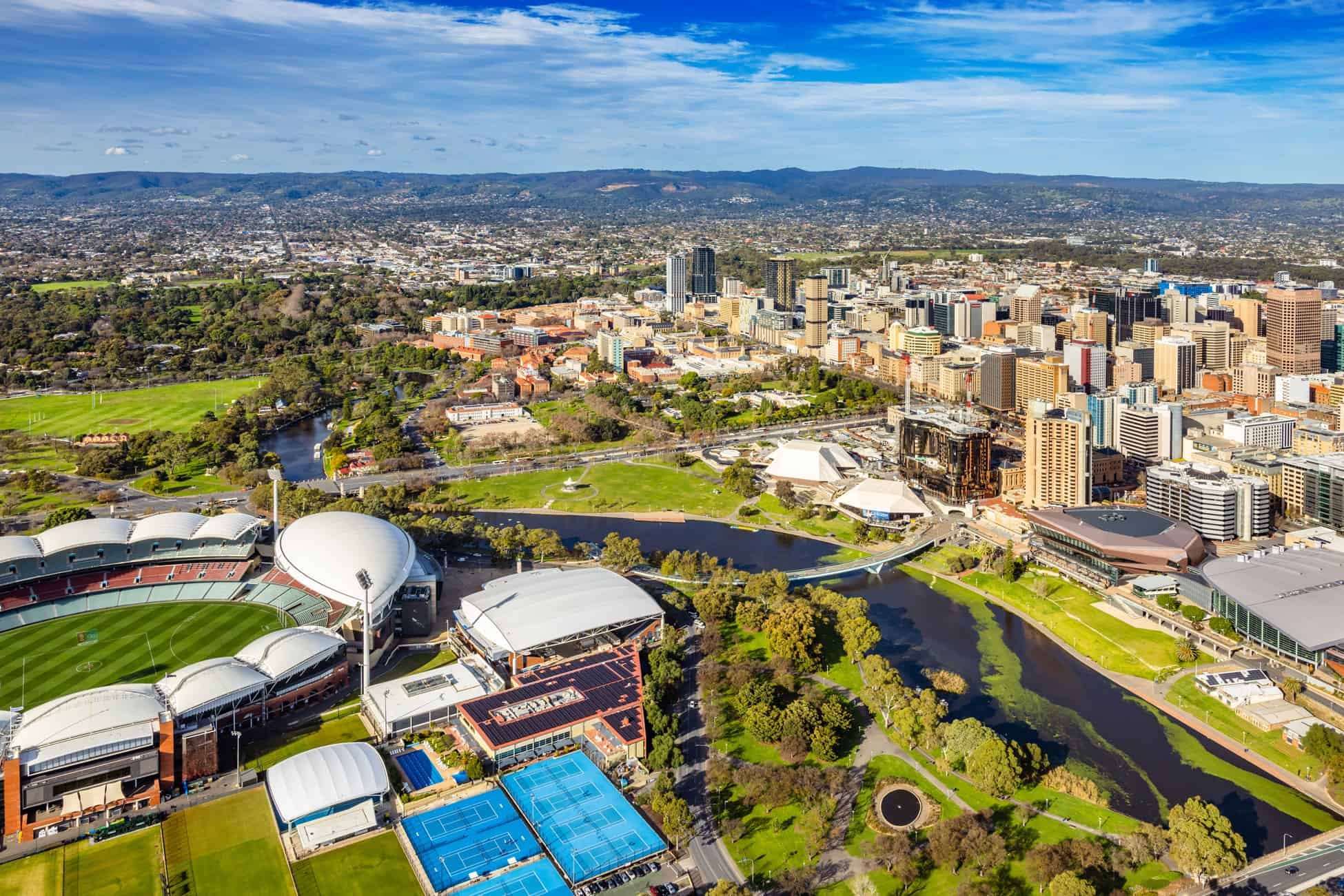 Aerial view of downtown Sacramento, California, showing sports stadiums, parks, rivers, and high-rise buildings under a blue sky.