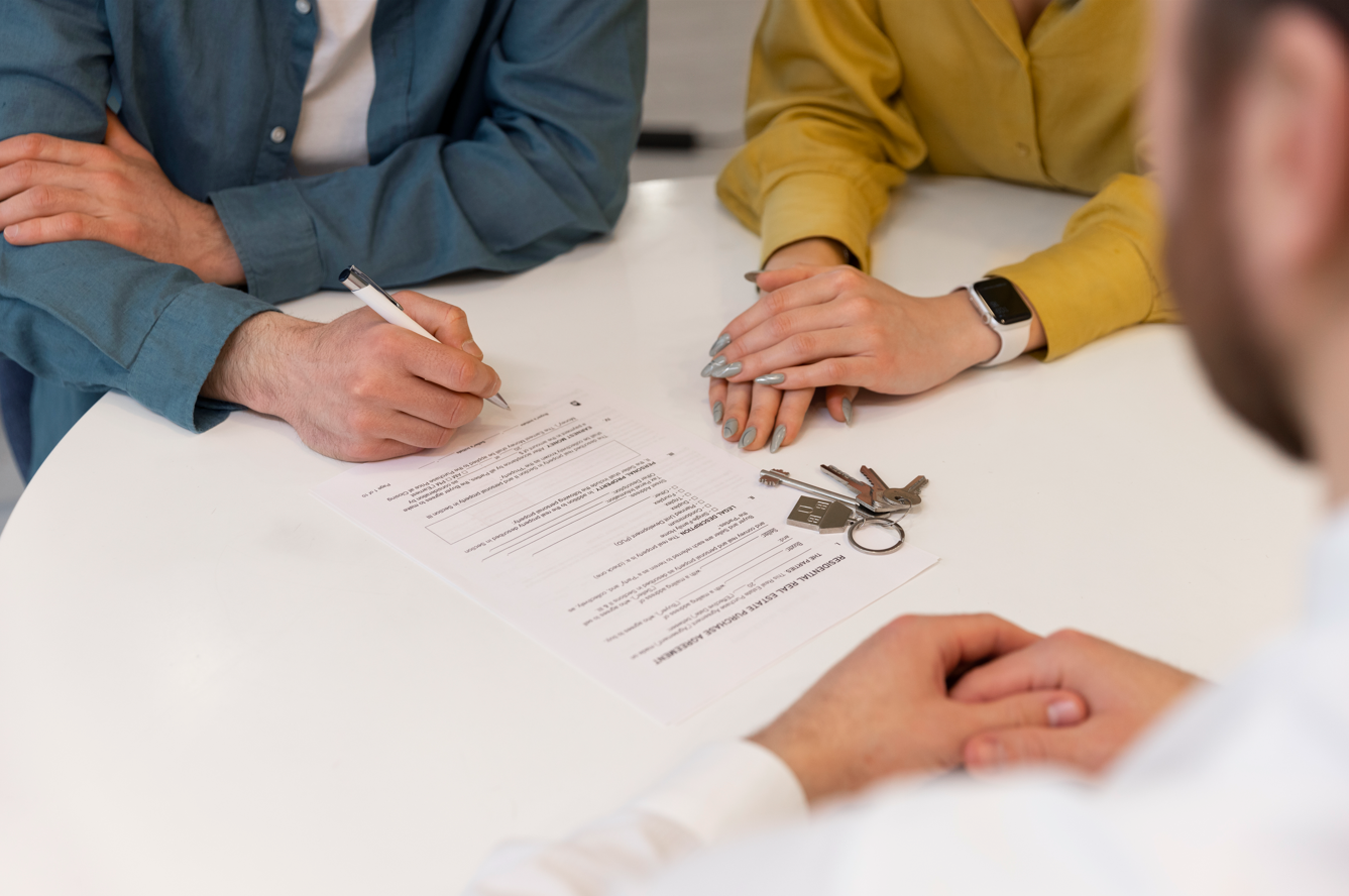 People signing a rental agreement or lease document at a table, with keys and a keychain placed on the table.