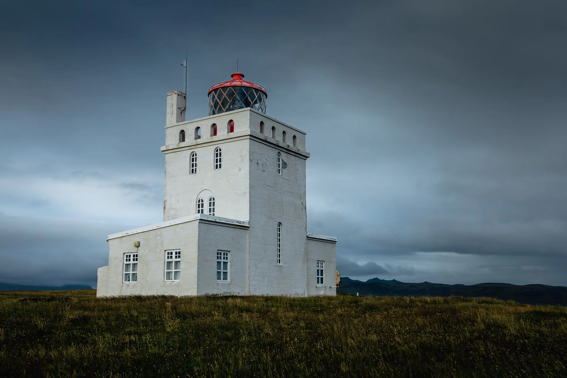 Moody fine art photography of Dyrhólaey Lighthouse in Iceland, high-contrast coastal architecture, minimalist atmospheric wall art.