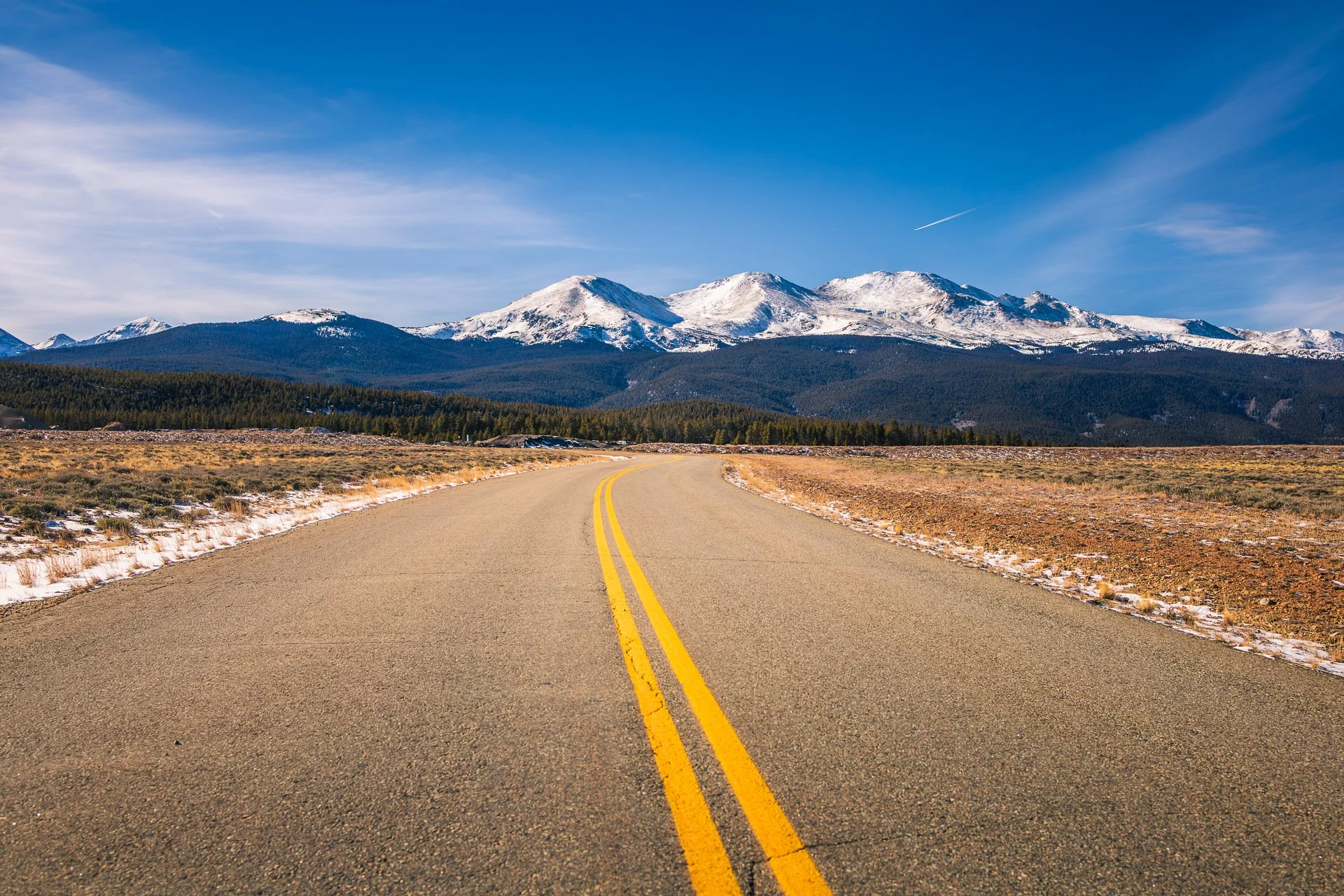 Long open road leading toward the snow-covered peaks of the Sawatch Range near Leadville, Colorado.
