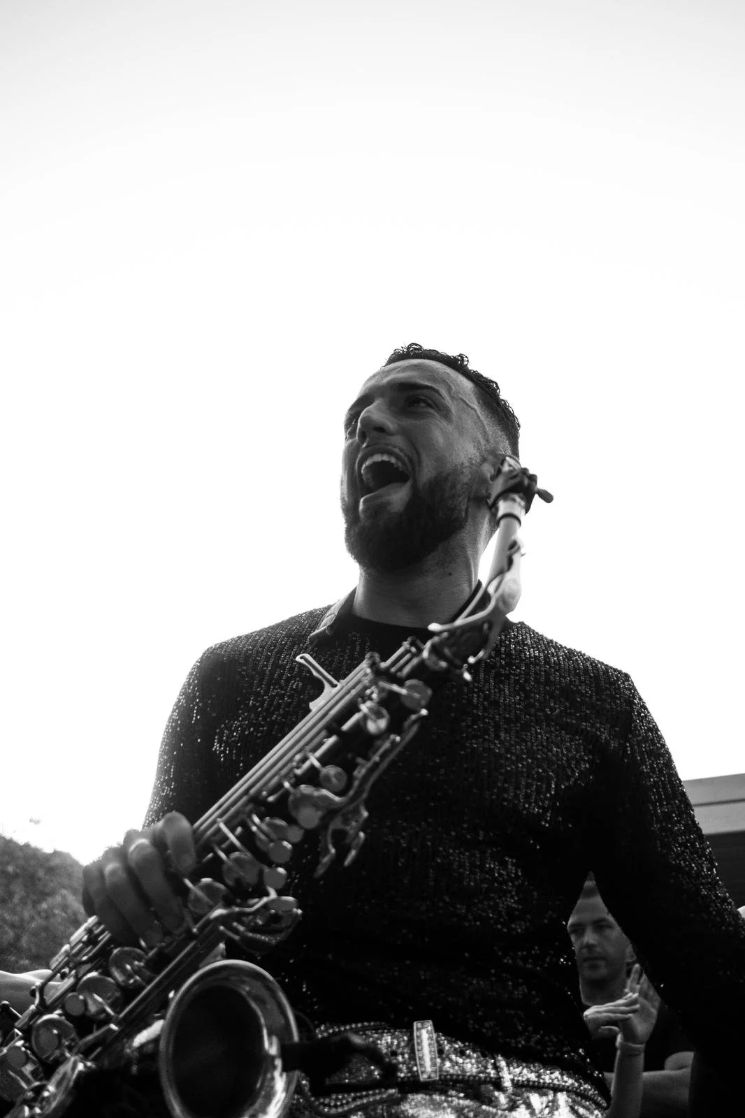 Un hombre tocando el saxofón, sonriendo y disfrutando la música, en un ambiente al aire libre.