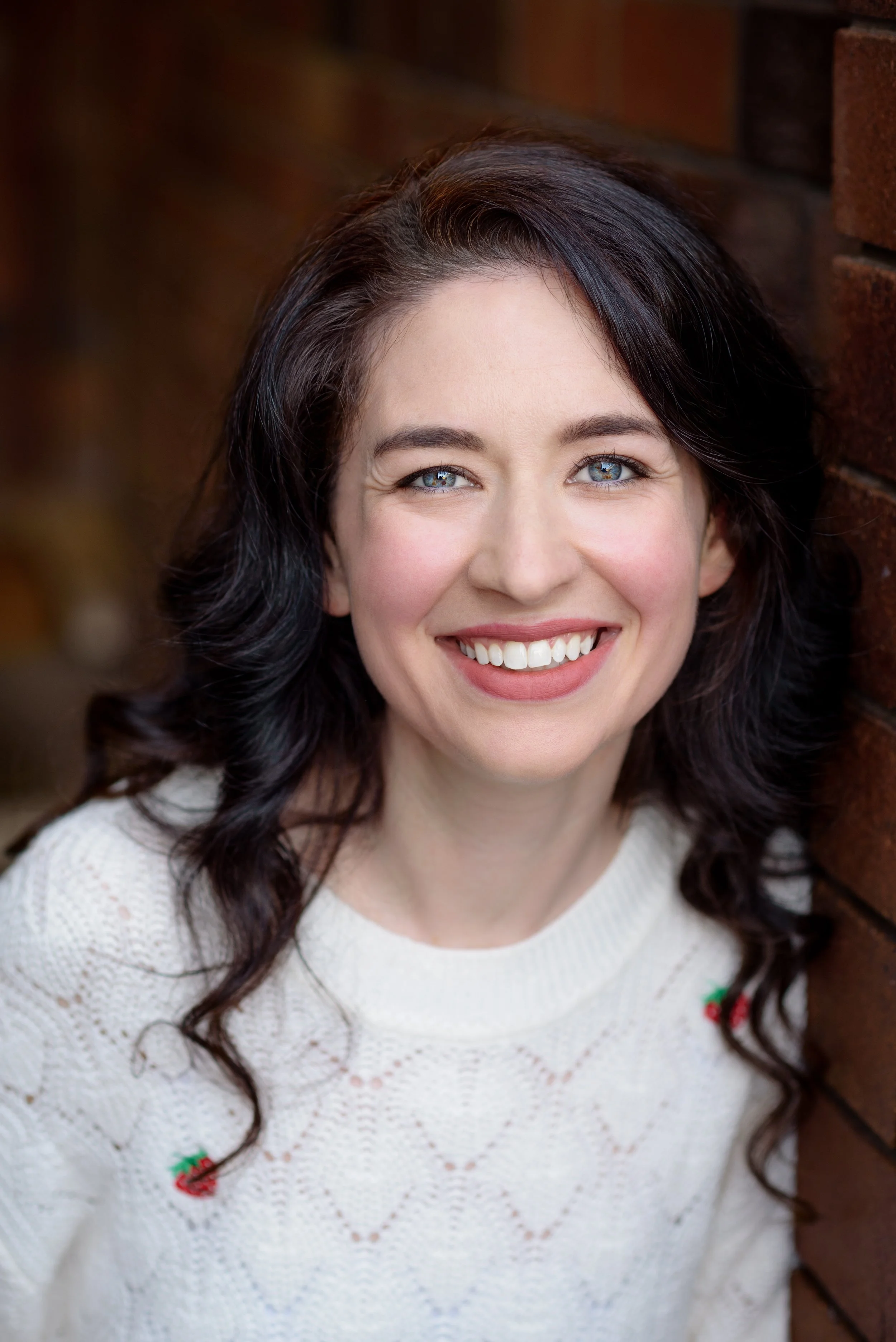 Sydney pianist Lauren Carey Kevin smiling directly at camera in casual white jumper next to brick wall