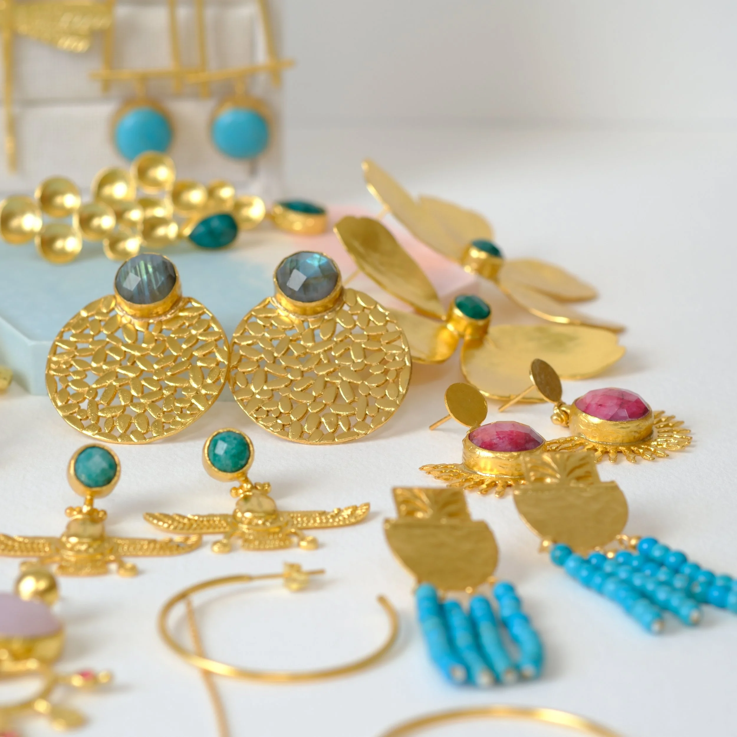 Collection of gold and gemstone jewelry including earrings, rings, and bracelets on a white surface.