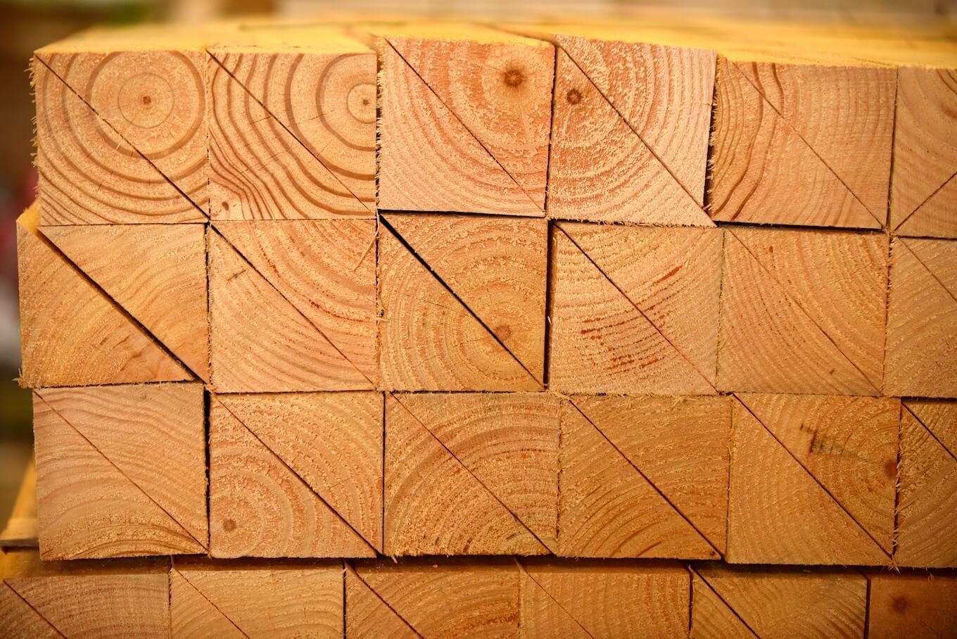 Stack of cut wooden planks with visible growth rings and diagonal cuts.