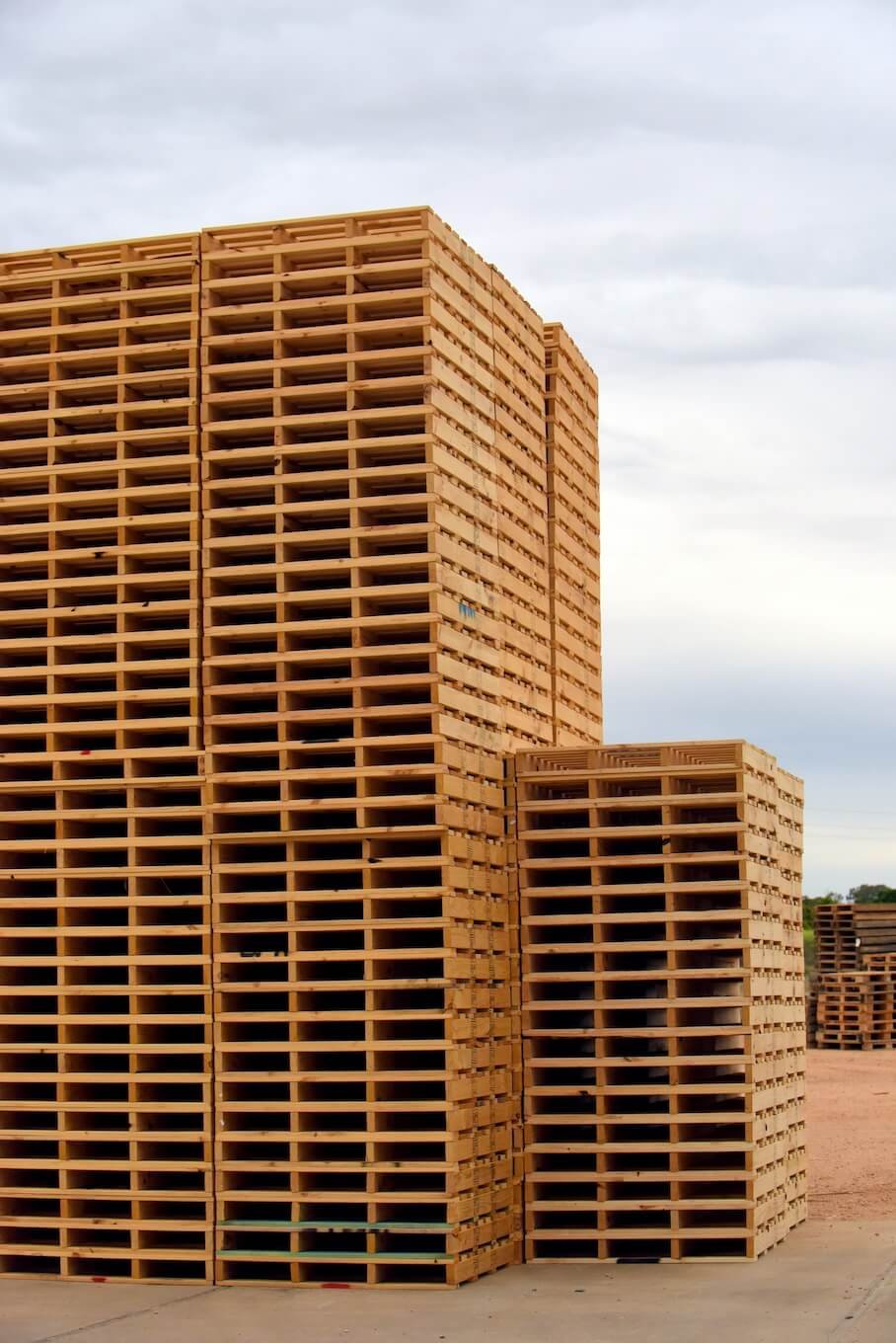 Multiple stacks of wooden pallets at an outdoor construction site against a cloudy sky.