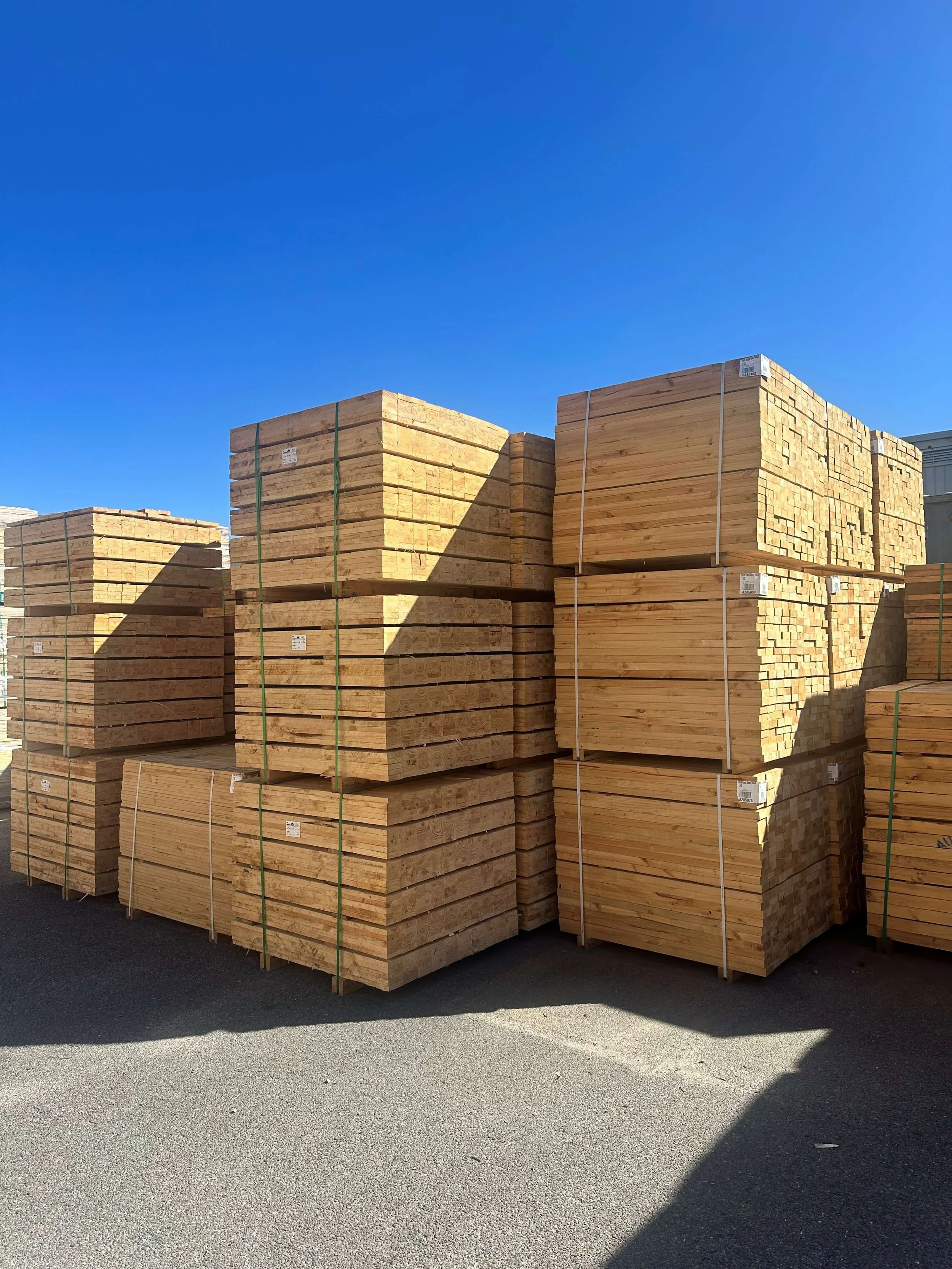 Stacks of wooden planks organized in pallets outside under a blue sky.