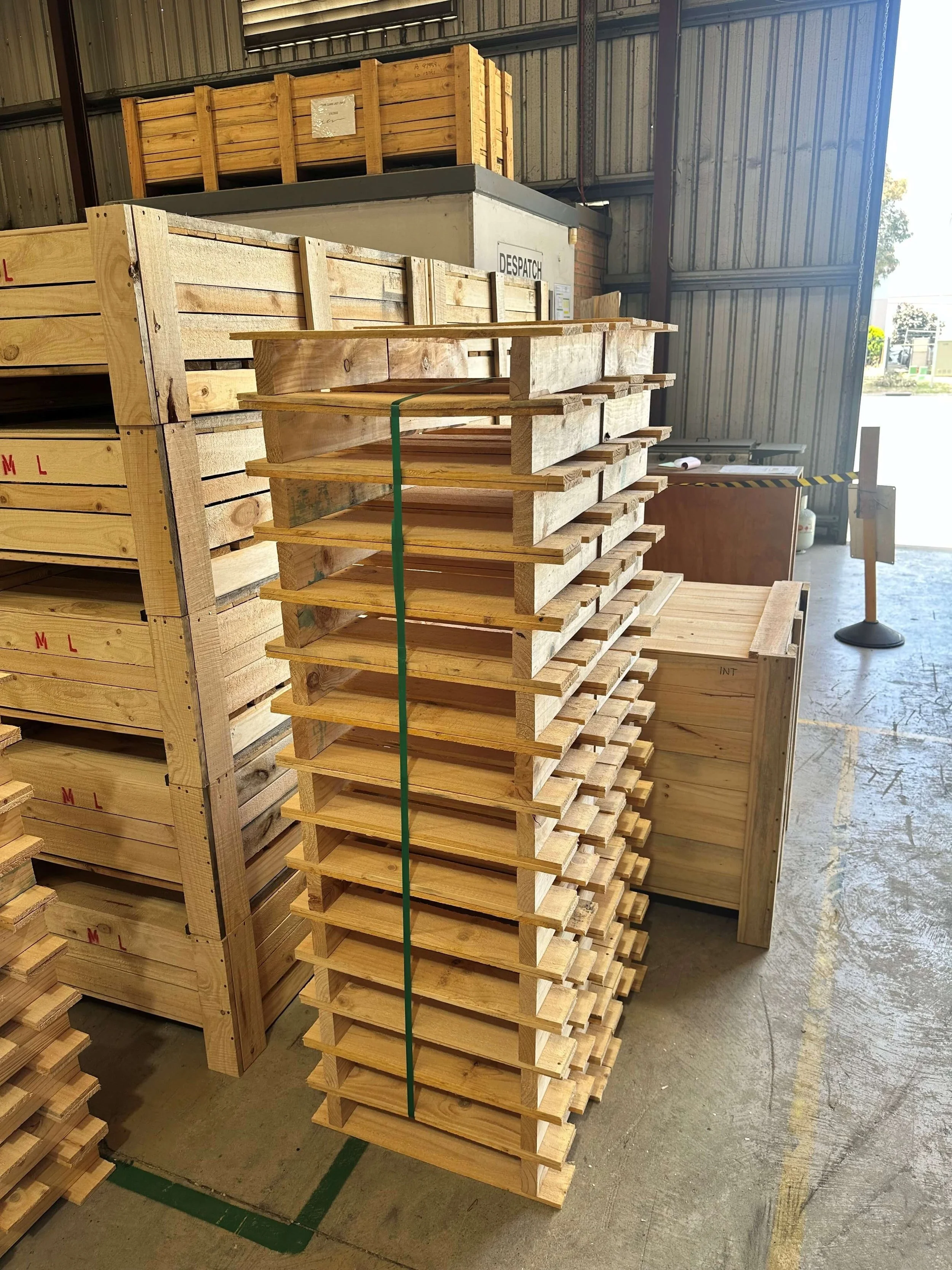 Stack of wooden pallets inside a warehouse with shelves and boxes in the background.