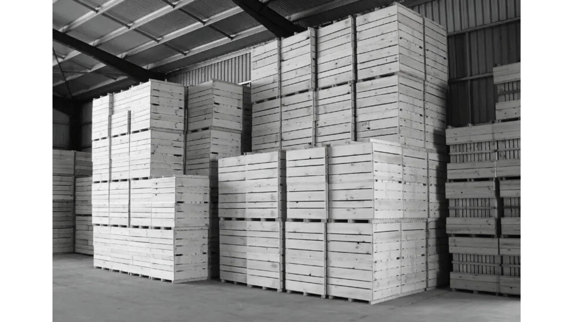 Stacks of wooden pallets inside a warehouse with metal roof and walls.