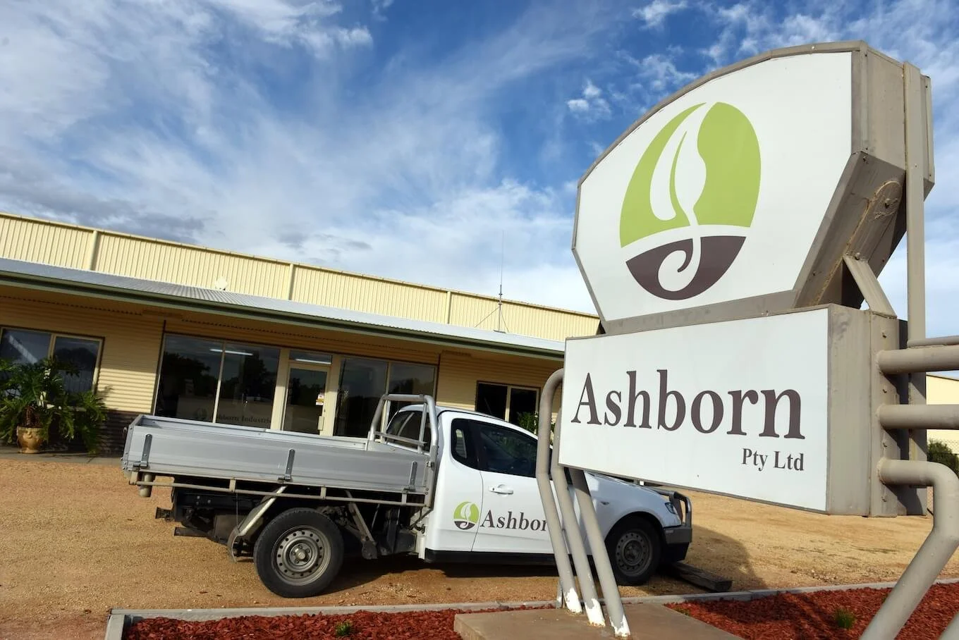 Modern house with large glass window, surrounded by yellow-green shrubbery, against a mountainous landscape in the background.