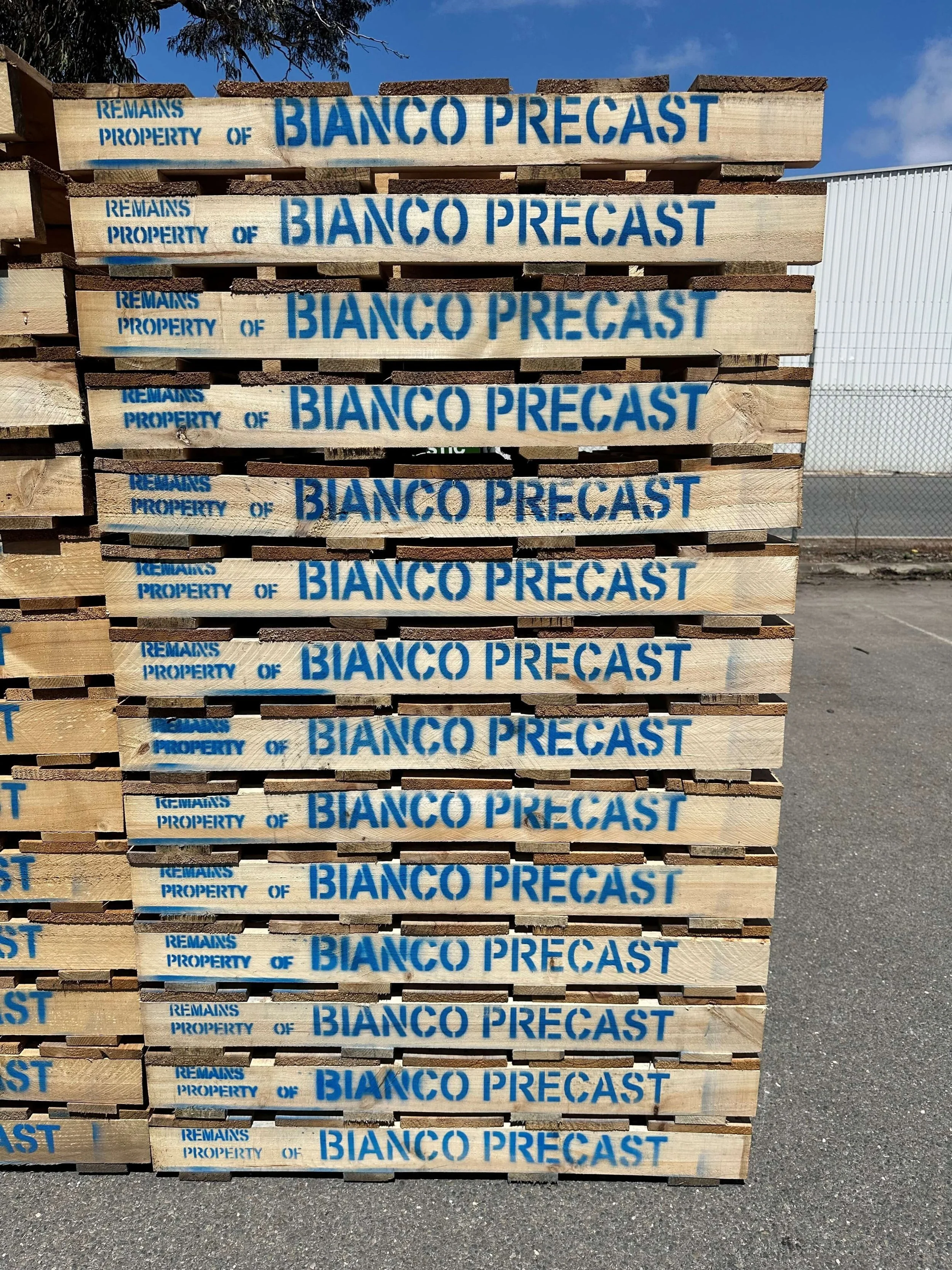 Stack of wooden pallets with blue stenciled text that reads 'Remains Property of Bianco Precast'.