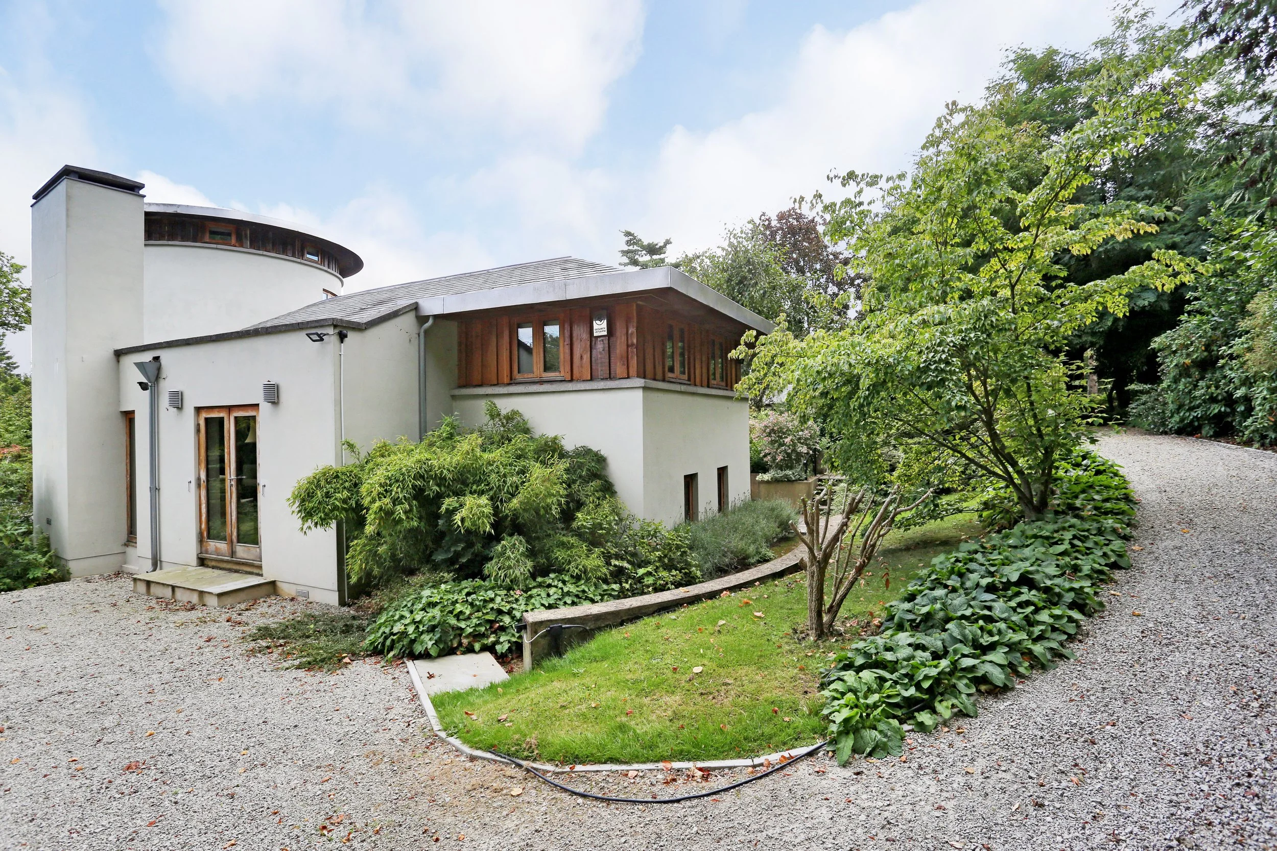Modern white building with curved architecture, wood-framed windows, landscaped garden, and gravel paths