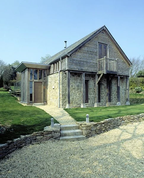 A two-story house with a stone and timber exterior, a small front balcony, and surrounded by a well-maintained lawn.
