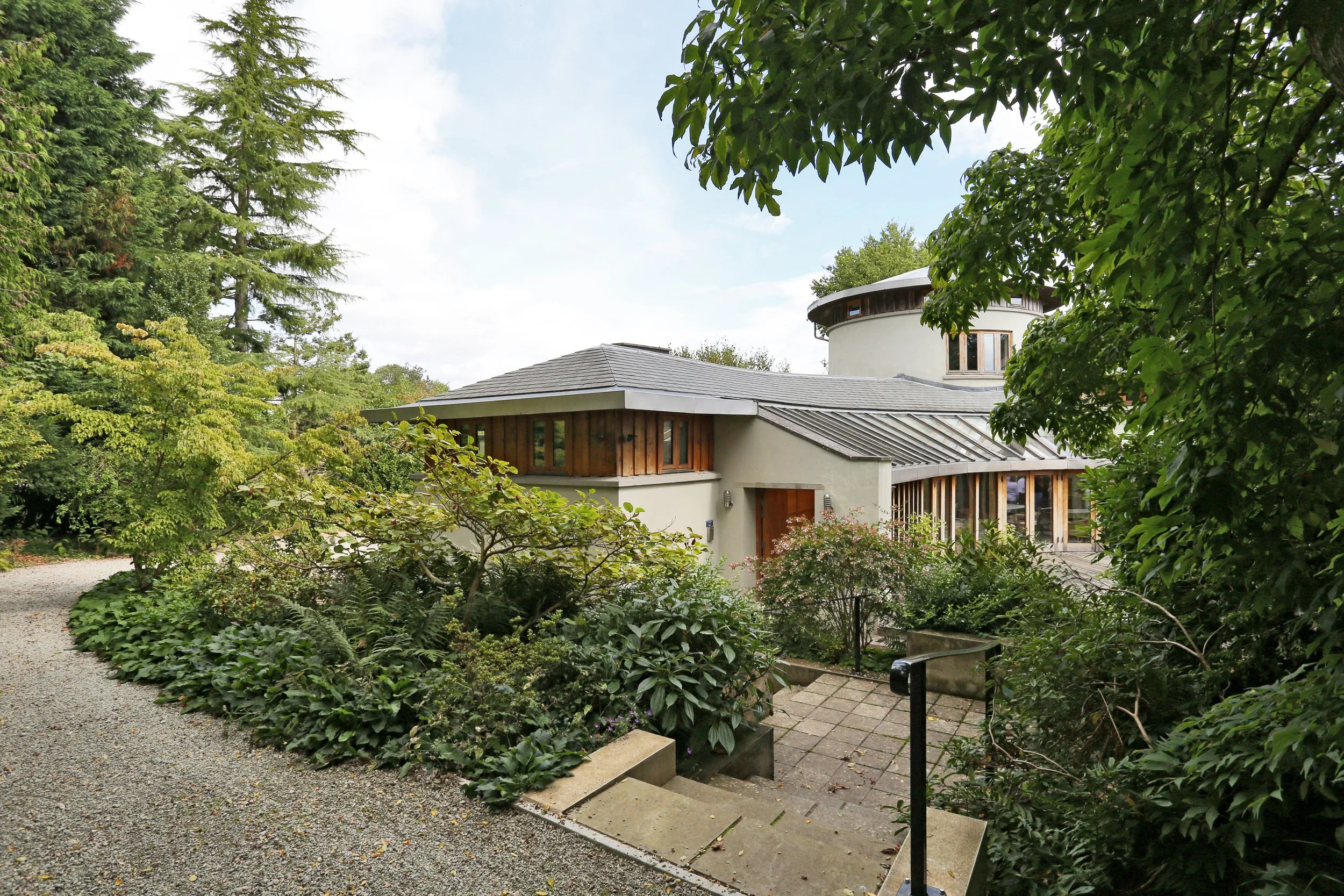 Modern house surrounded by lush gardens, trees, gravel paths, and landscaped steps