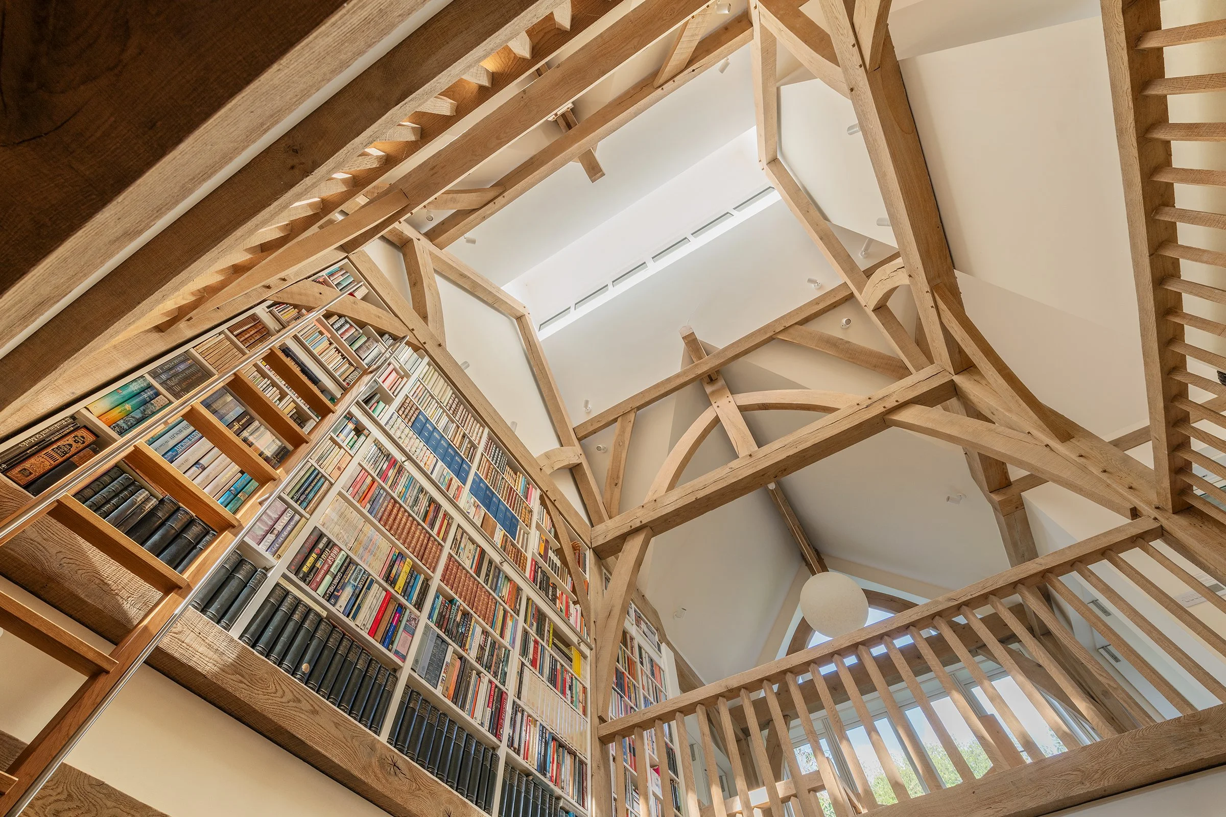 Looking up through an oak framed library space, with top lighting and lots of coloured books.