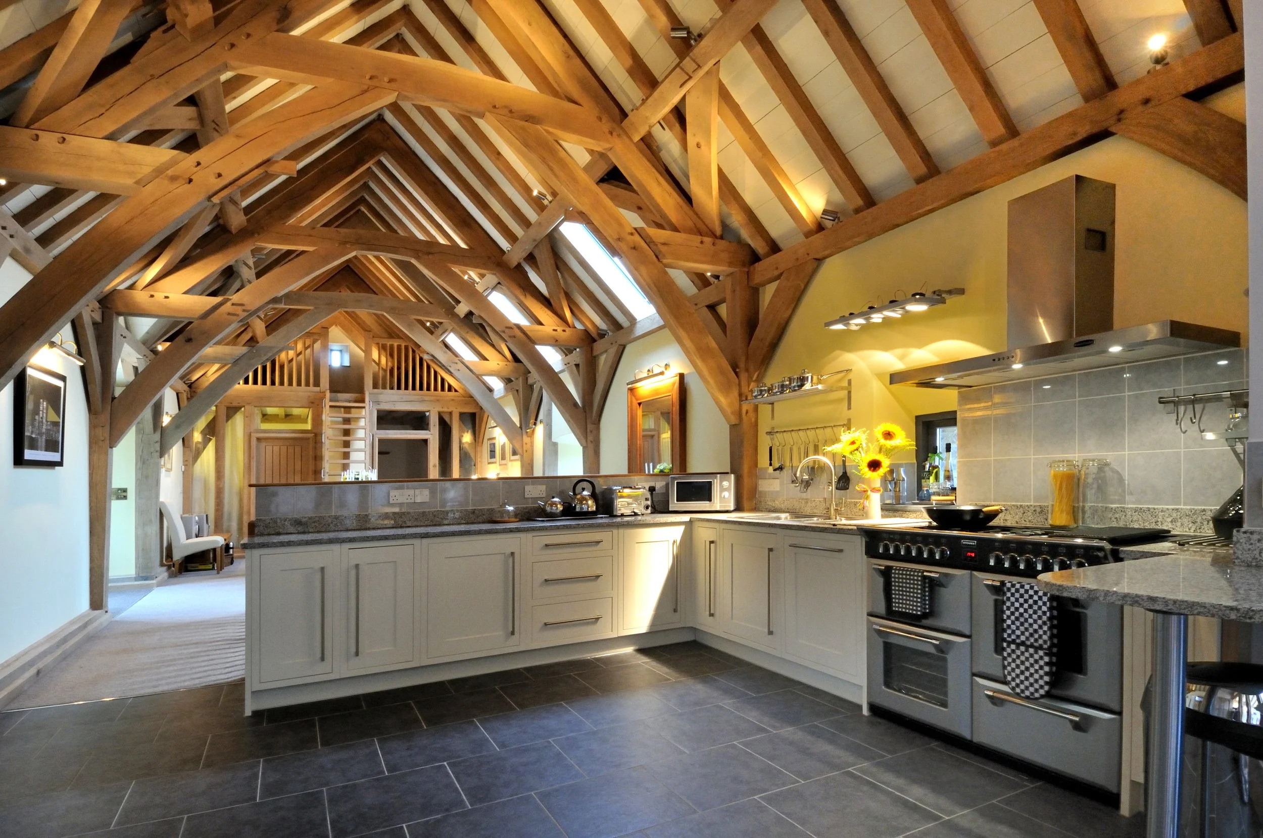 Kitchen with exposed wooden beams on the ceiling, white cabinets, gray countertops, a stove, a microwave, and a vase of sunflowers.