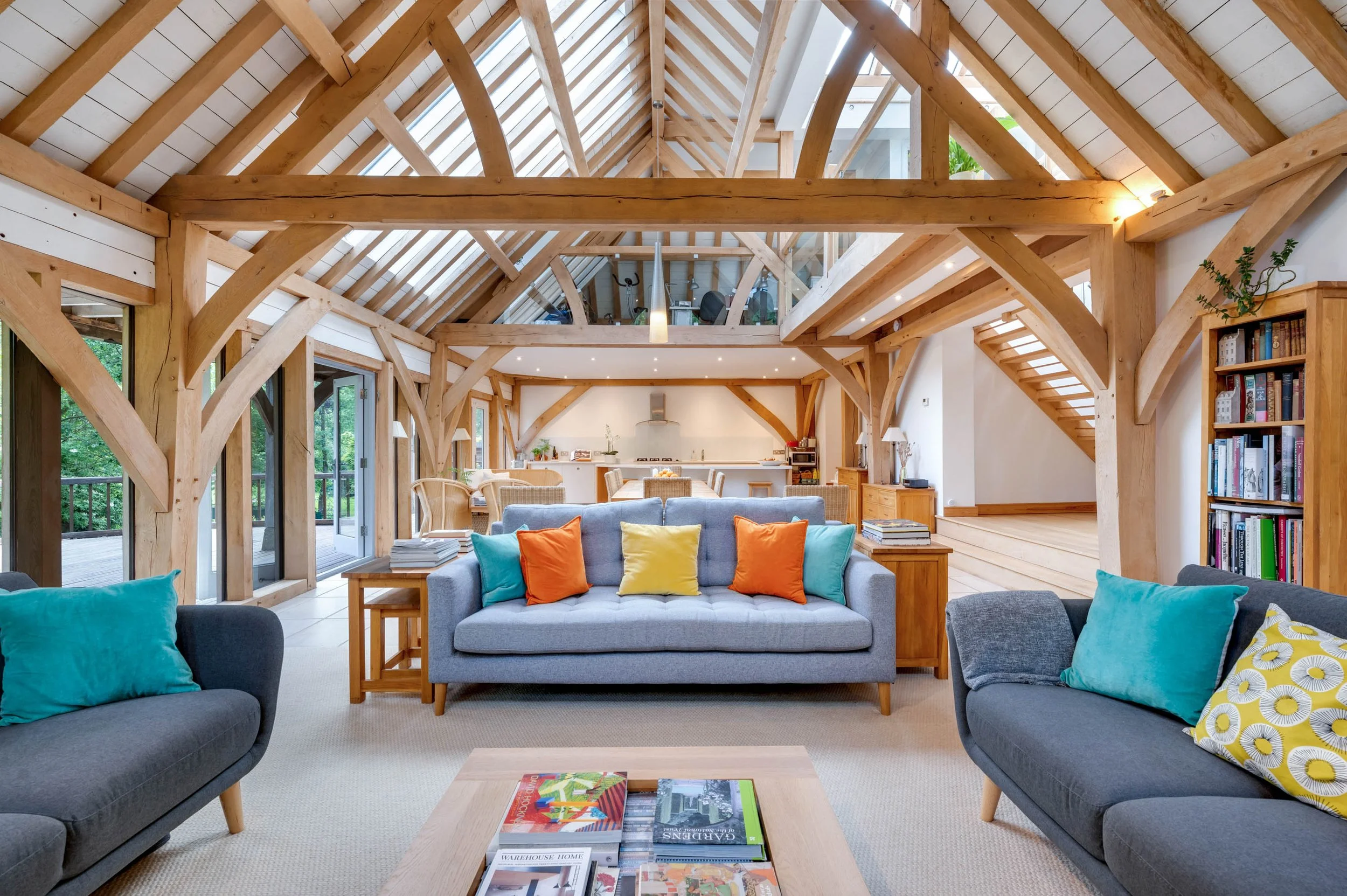 Spacious living room with oak beams, large windows, gray sofas with colorful pillows, and a coffee table with magazines.