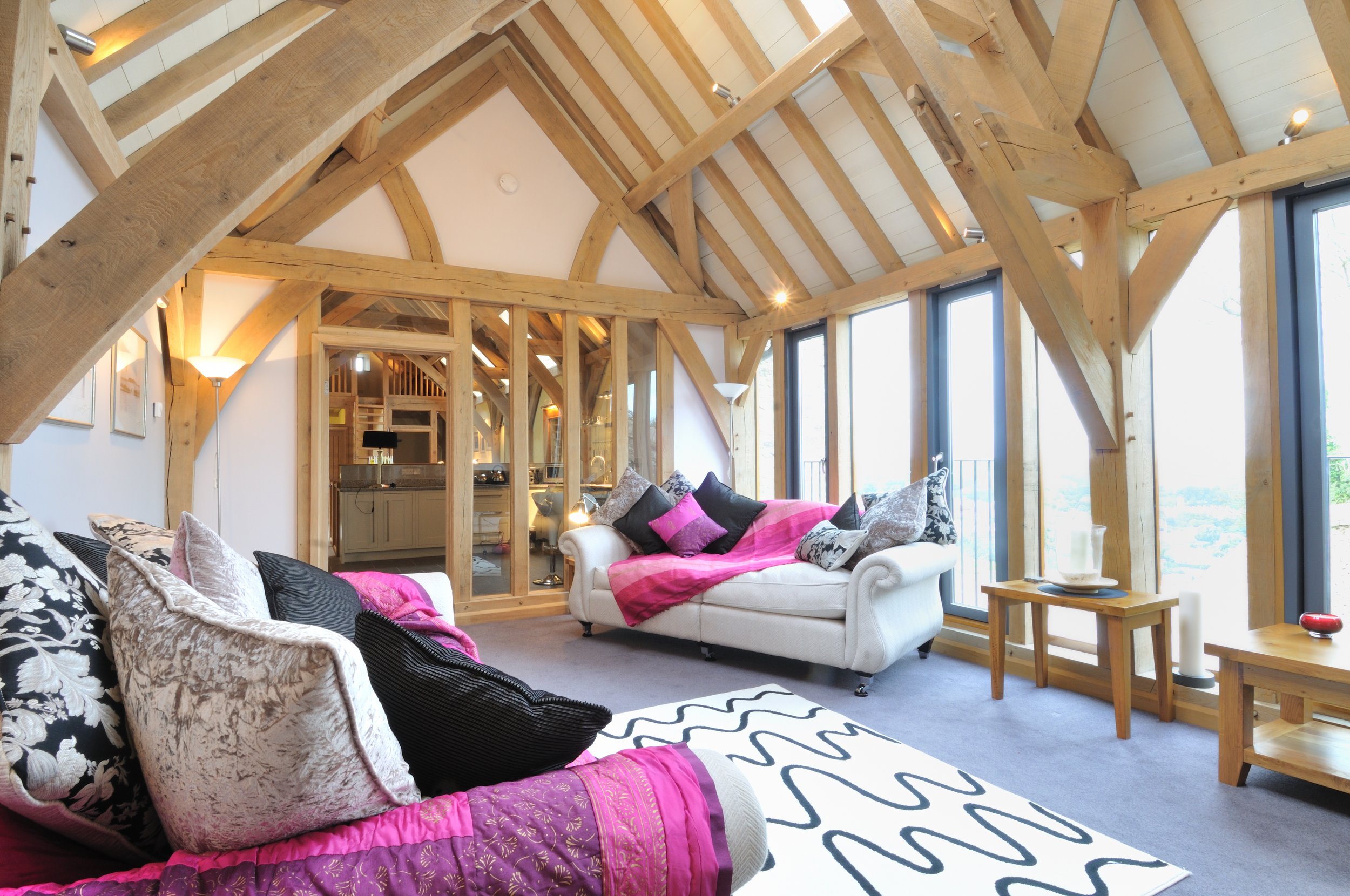 Living room with white sofas, patterned pillows, pink throw blanket, wooden beams, and large windows.