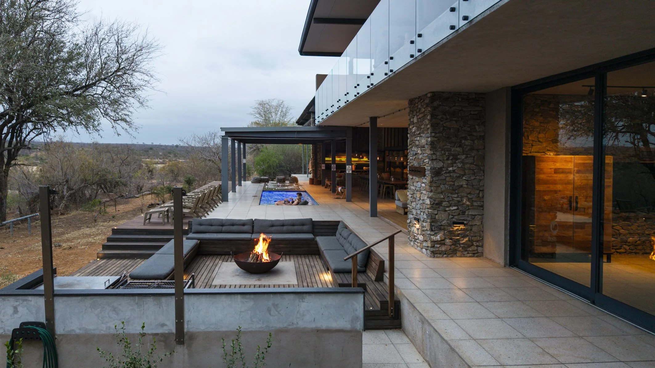 Modern house with outdoor patio, pool, fire pit, and scenic landscape with trees in the background