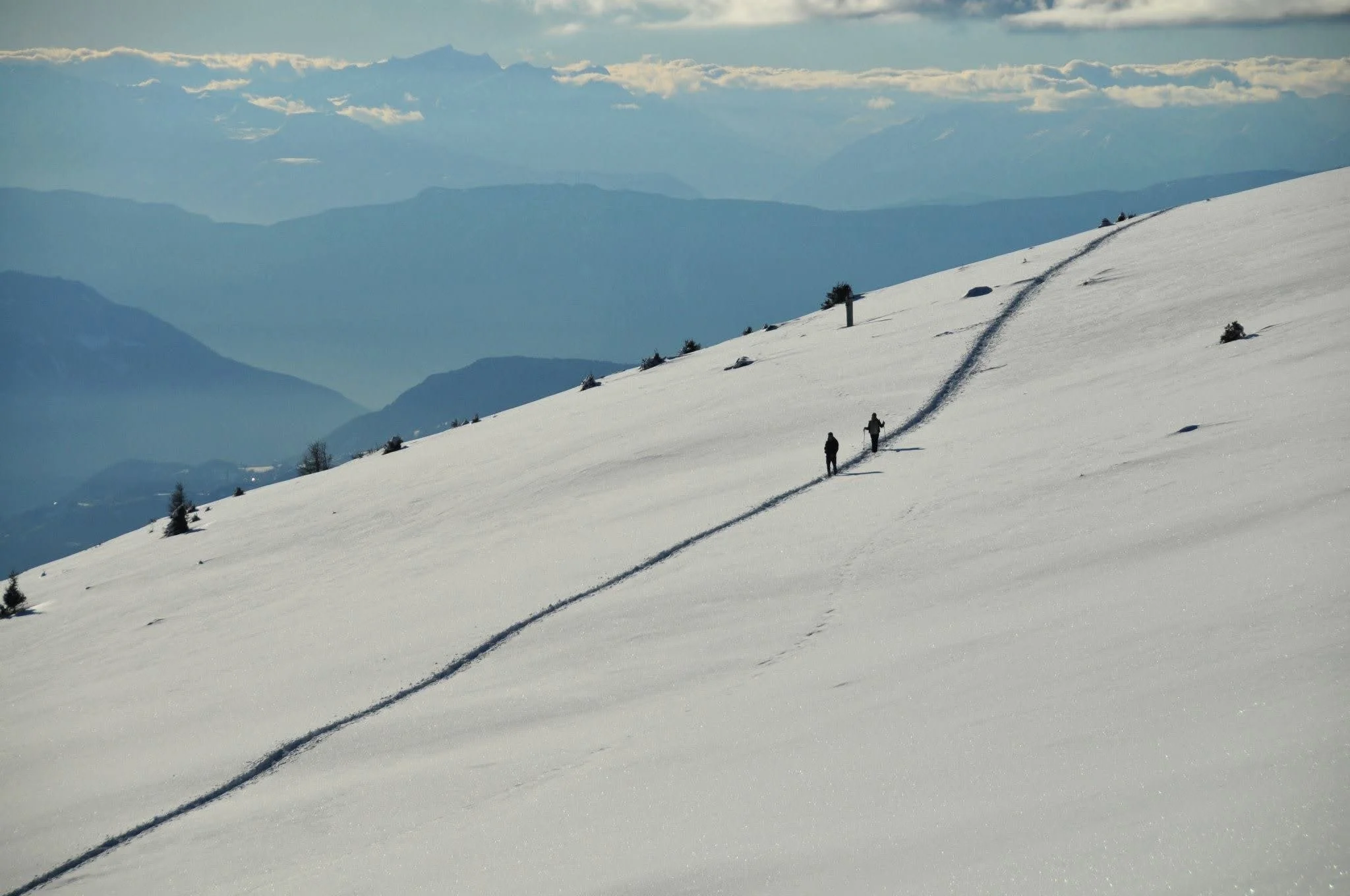 Winter hikers walking along a snowy mountain slope in the Dolomites with layered alpine peaks in the distance